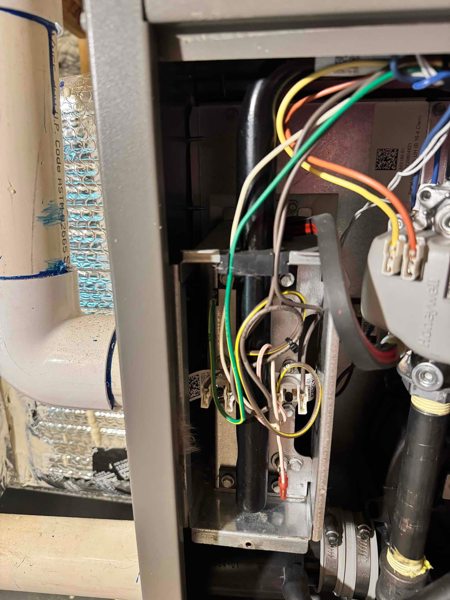 Furnace cabinet open, showing wiring harness, pressure switch, and PVC vent piping alongside internal components and mounting bracket.