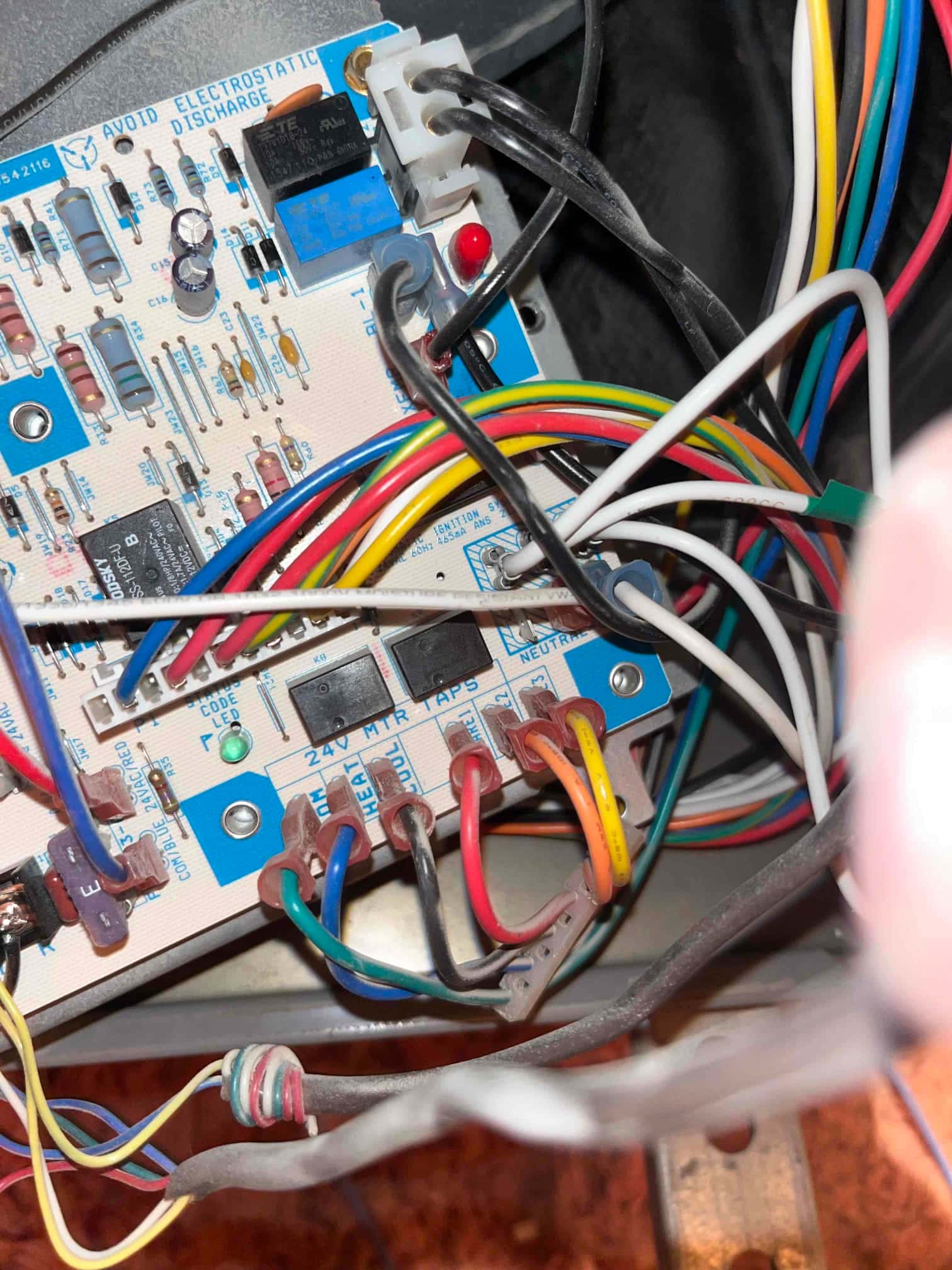 HVAC control board inside the air handler showing terminal labels, relays, two status LEDs, and multiple connected colored wires.
