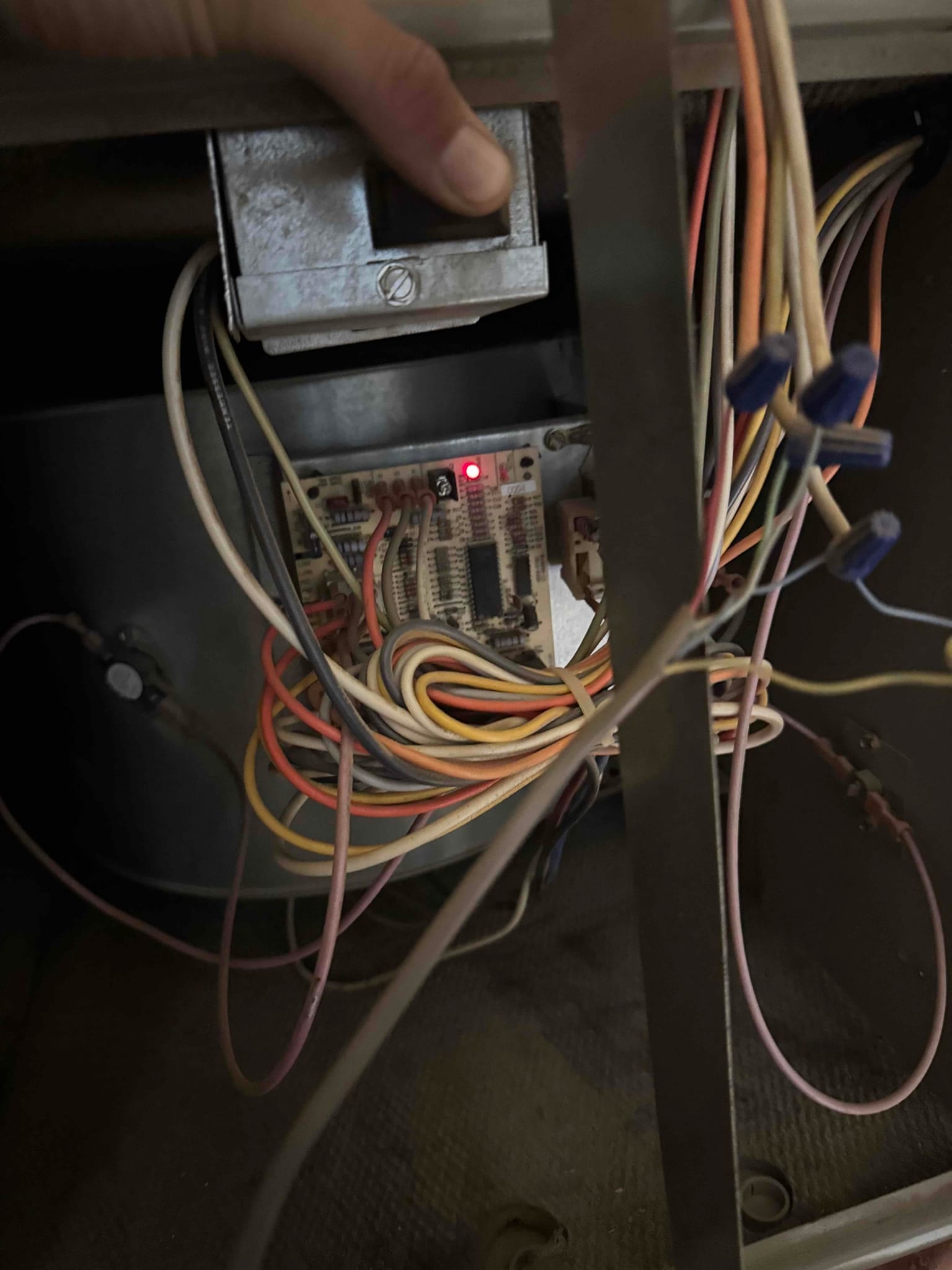 HVAC control board with multiple wires connected, red status LED illuminated, and wire nuts securing splices inside the unit.
