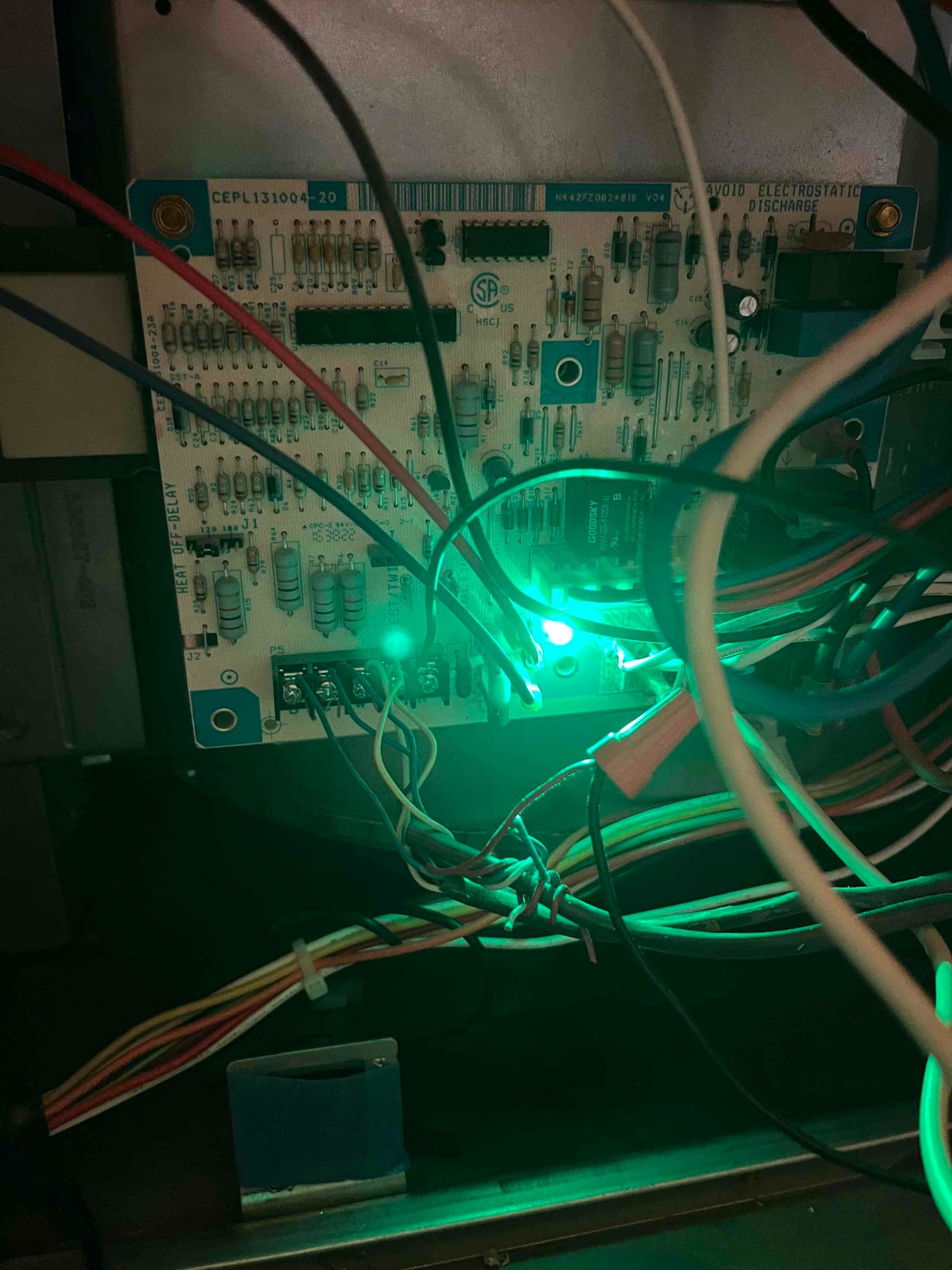 HVAC control board with wiring connected and two green status LEDs illuminated inside the unit.