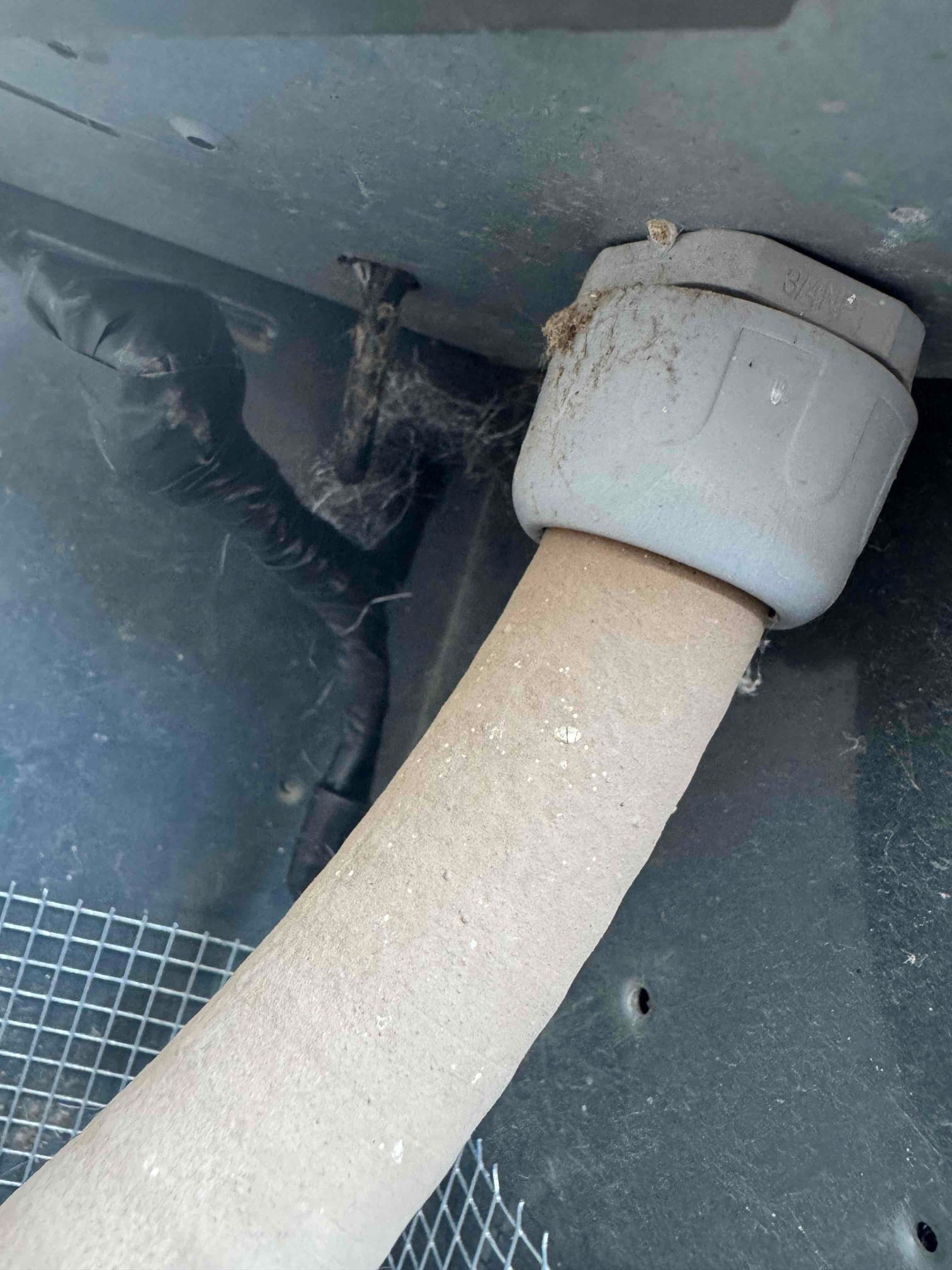 Insulated refrigerant line passes through a plastic bushing into the outdoor unit cabinet, with adjacent taped tubing and debris.