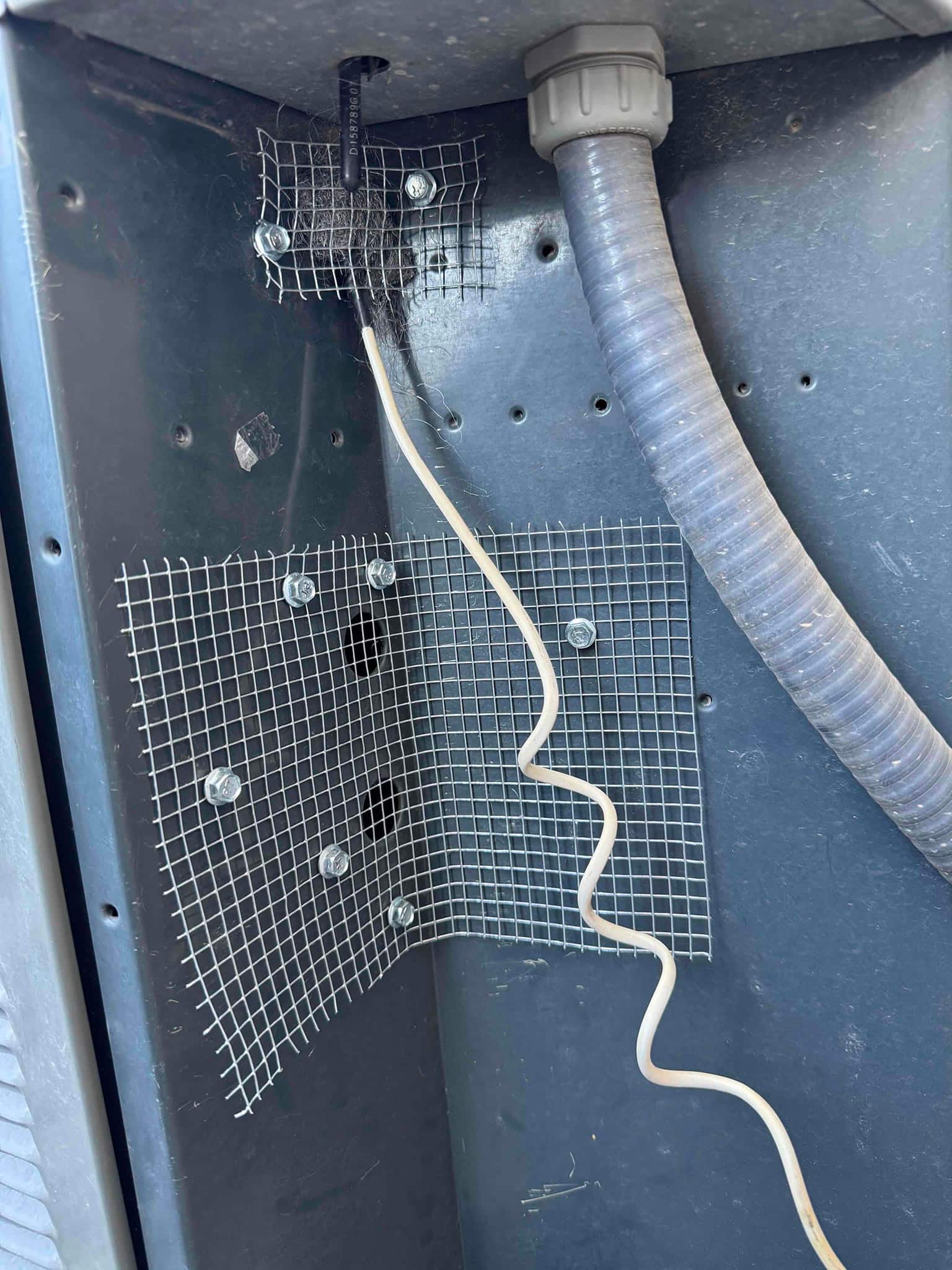 Interior condenser cabinet shows metal mesh panels fastened over openings, with flexible electrical conduit and a white control wire routed along the panel.