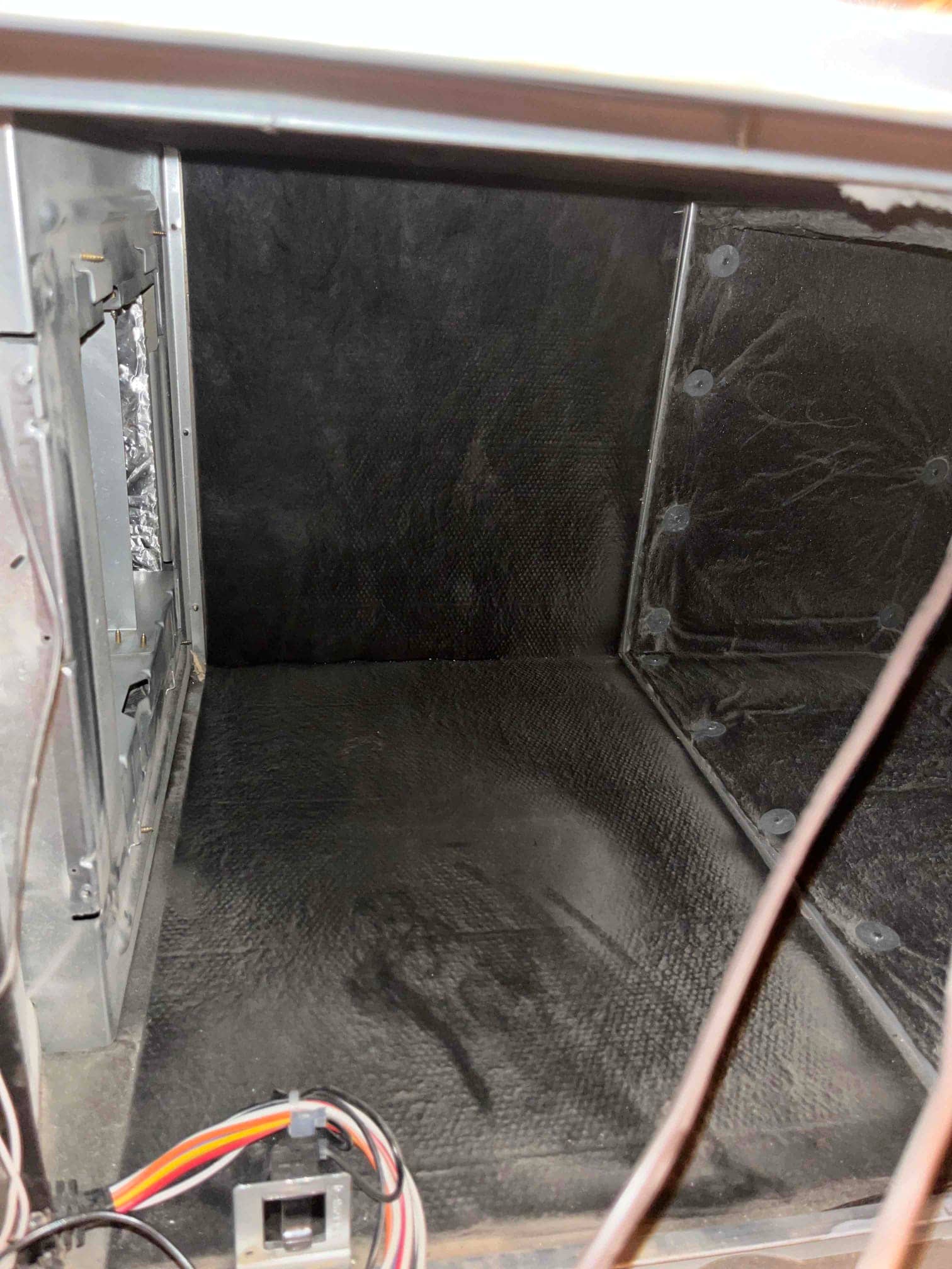 Interior of an HVAC air handler cabinet with black internal insulation and a small wiring harness at front.