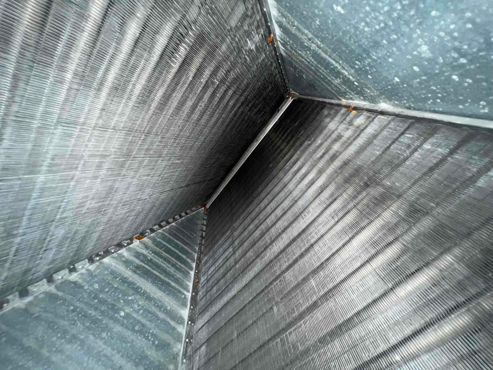 Interior view of an A-coil evaporator assembly with clean aluminum fins and light rust at fasteners.
