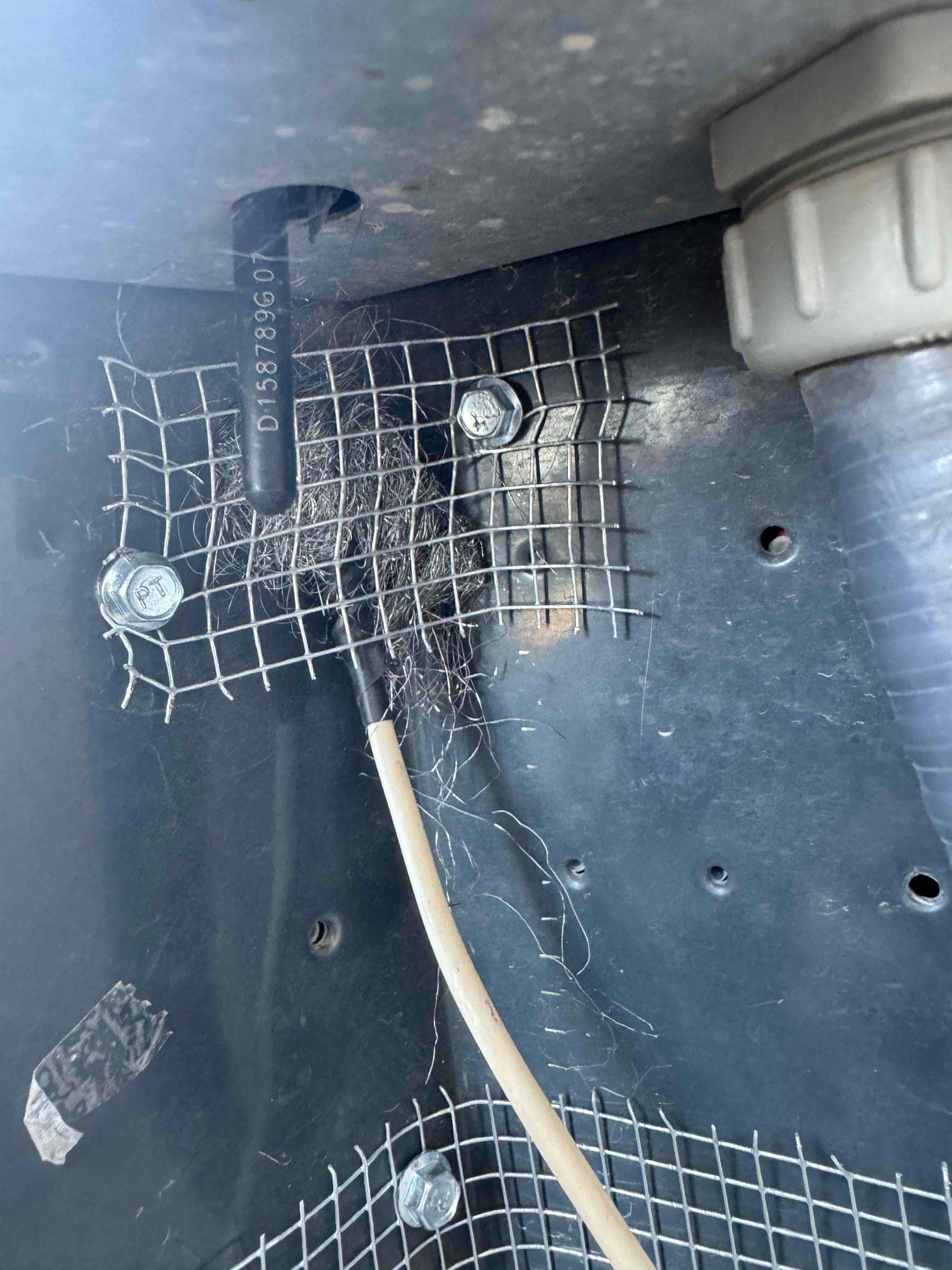 Metal mesh screens fastened inside unit cabinet around openings, with debris caught near wiring and conduit.