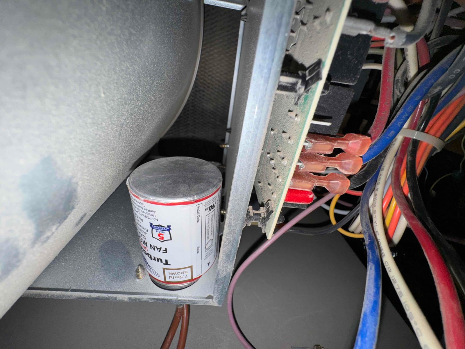 Motor run capacitor sits on cabinet floor beside control board connectors and bundled low-voltage wiring.