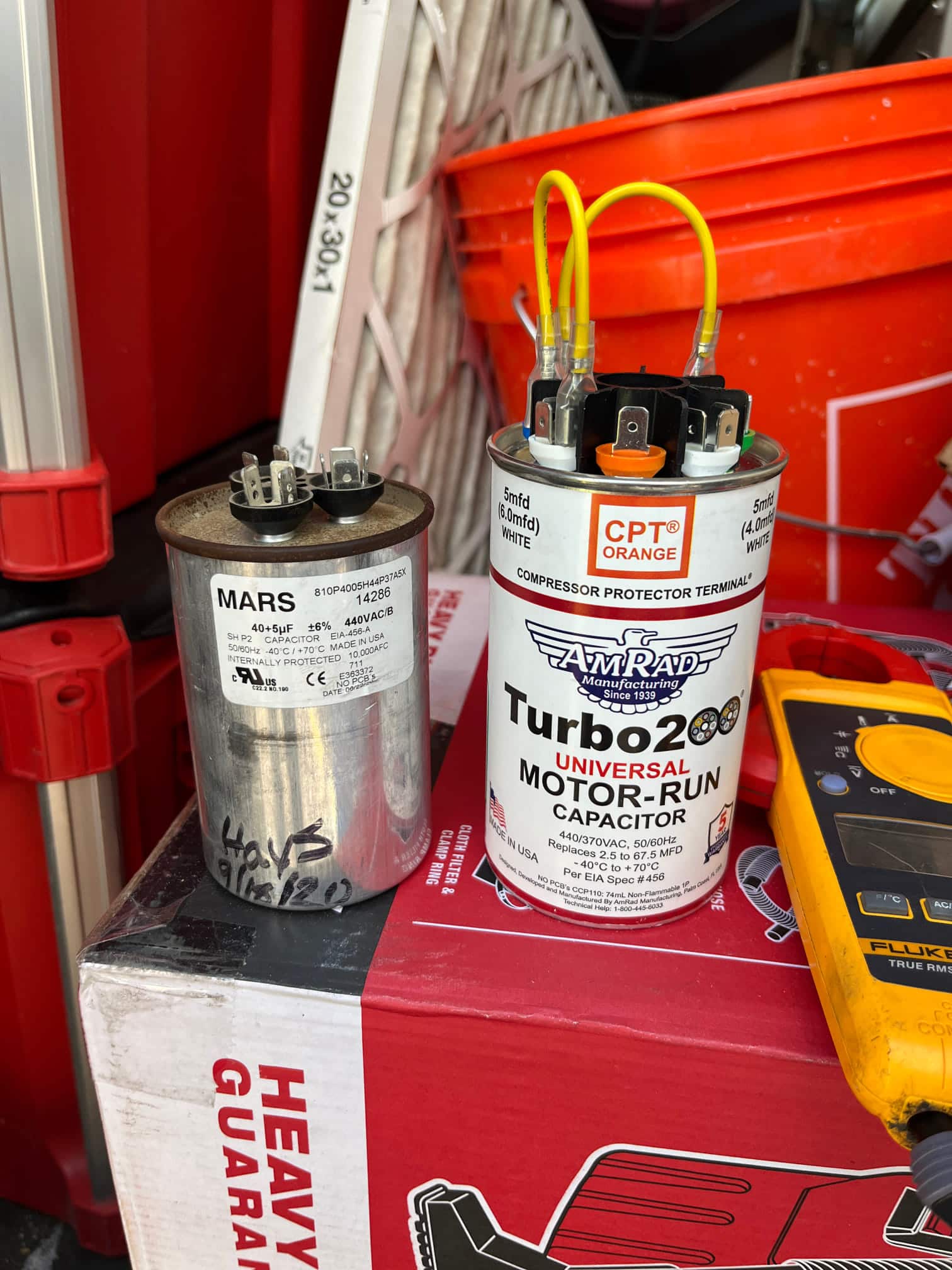 Two motor-run capacitors on the jobsite; one labeled 40+5 μF, the other universal with multiple terminals and jumpers.
