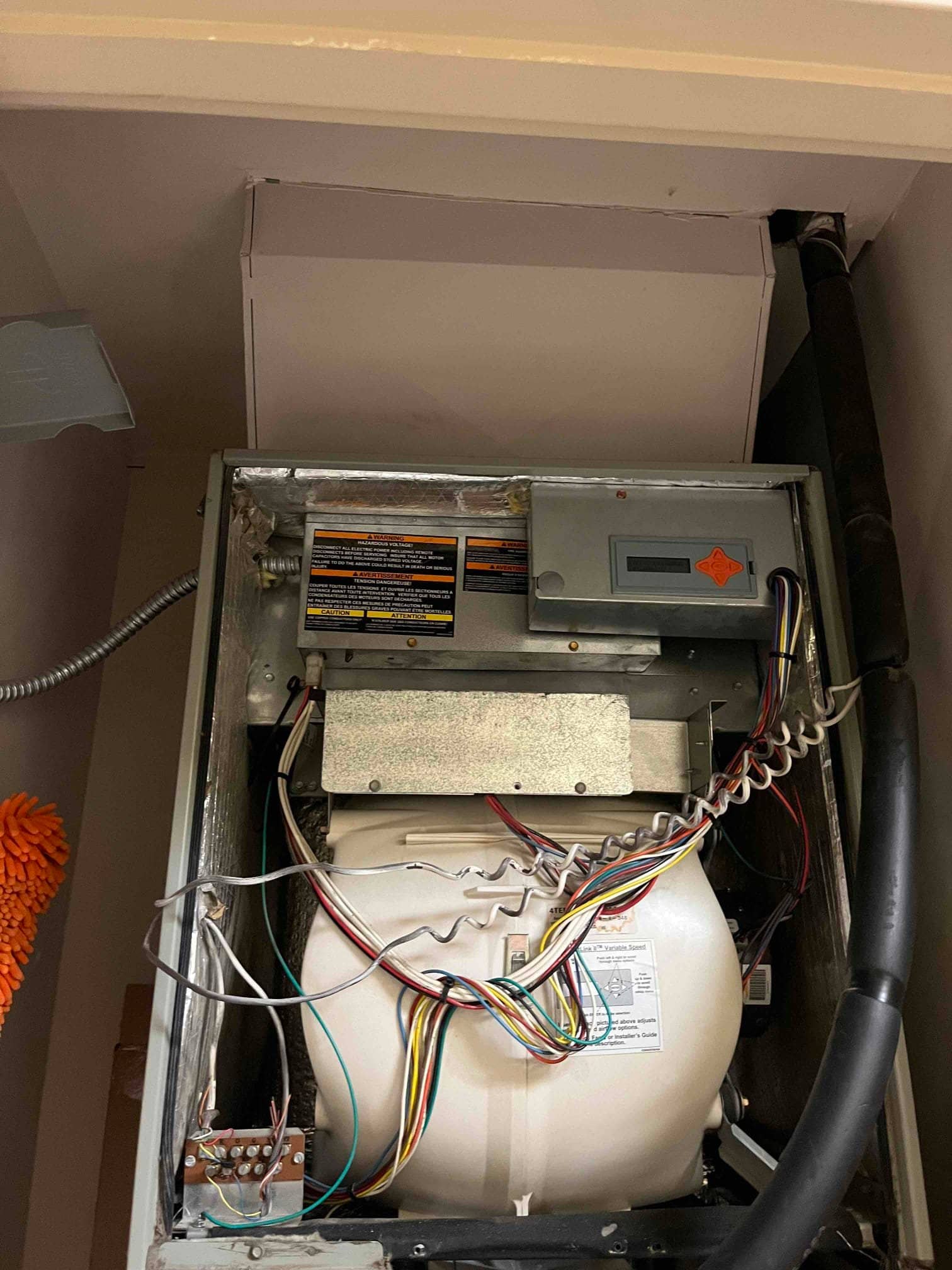 Open air handler cabinet showing blower housing with multicolor wiring, control compartment cover, and insulated refrigerant line at right.