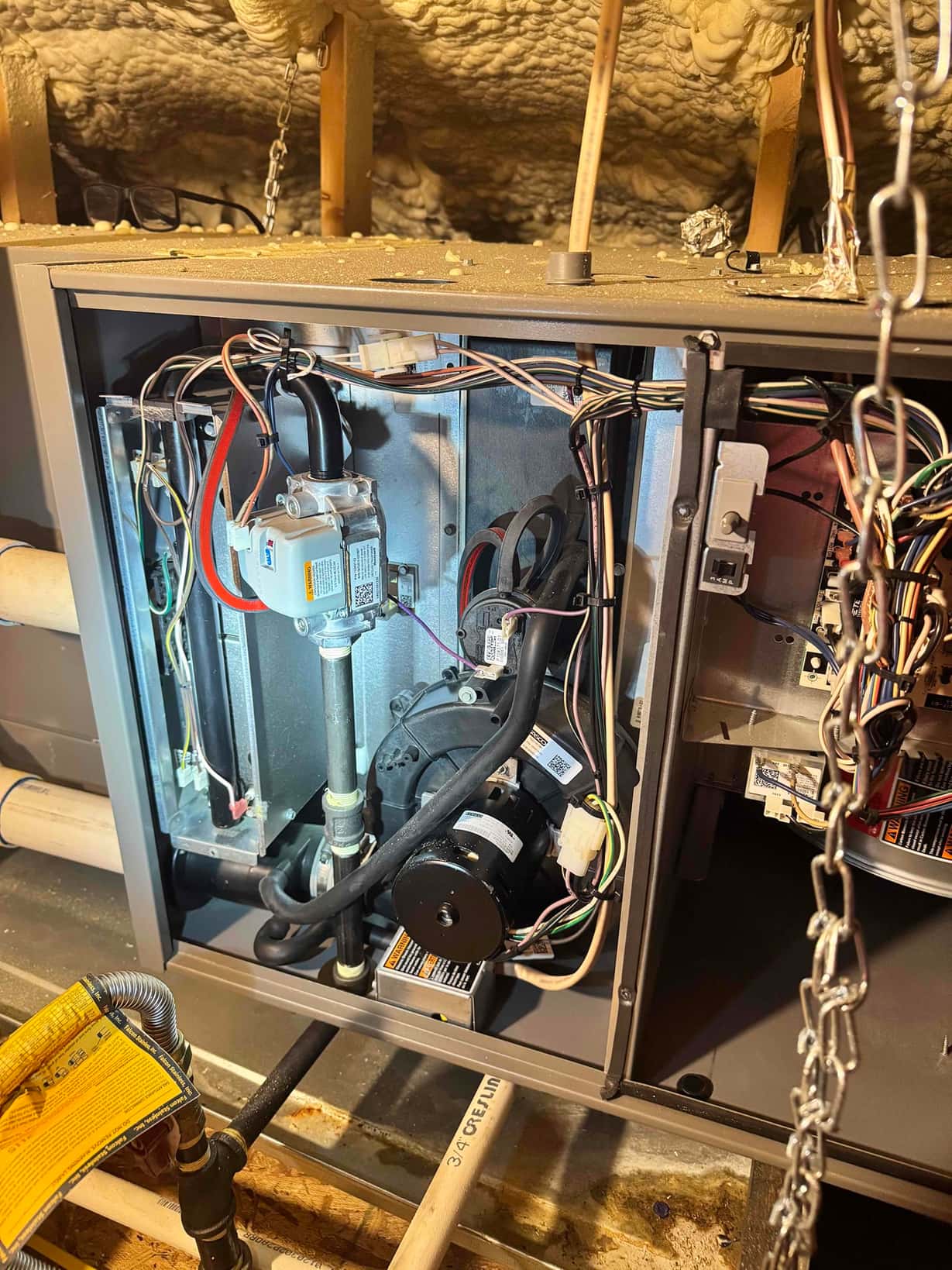 Open gas furnace cabinet showing inducer motor, gas valve, control wiring, and PVC condensate drain piping.