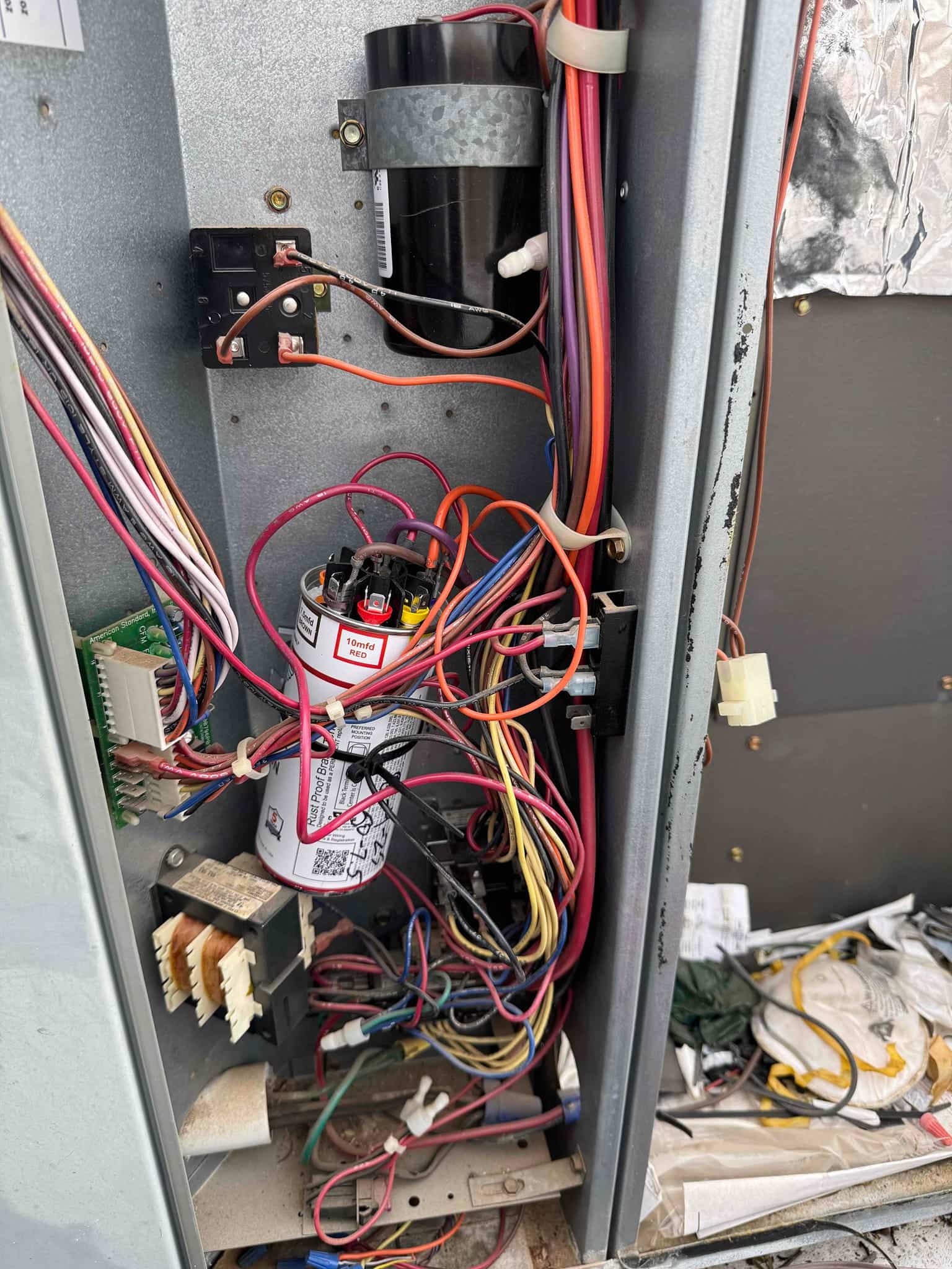 Open HVAC control compartment showing wiring, two capacitors secured to the panel, a transformer, relay blocks, and harnessed conductors.