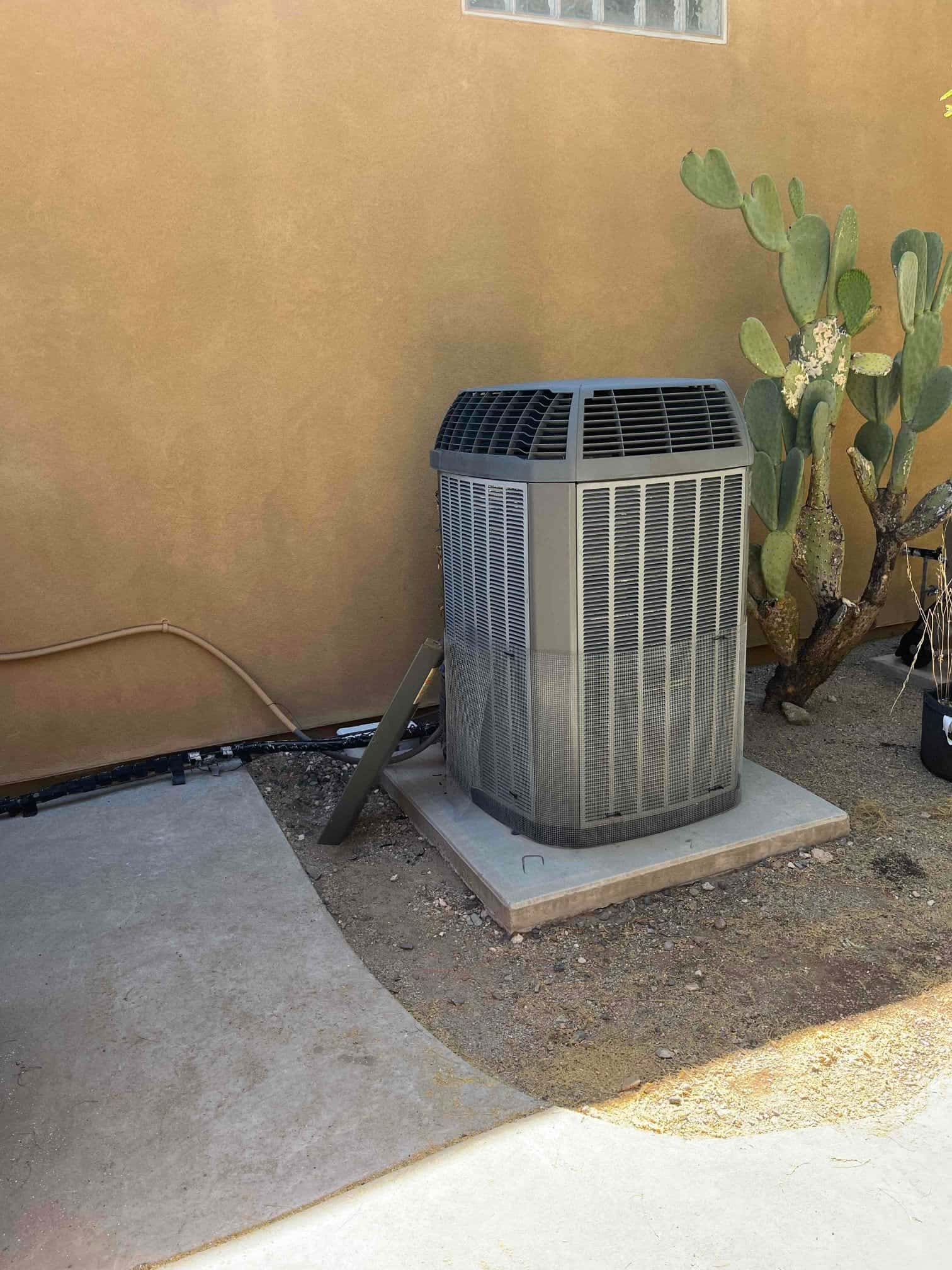 Outdoor air conditioning condenser sits on a concrete pad beside the wall, with insulated refrigerant line running to the house.