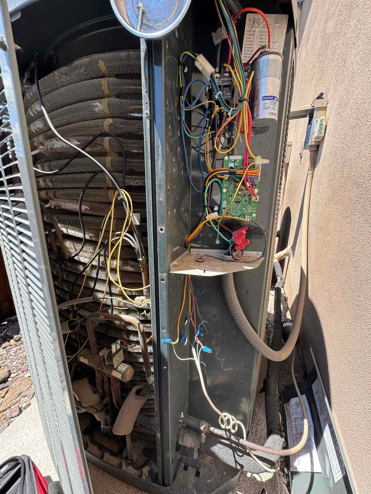 Outdoor condenser cabinet open, showing coil, control board, dual-run capacitor, and wiring with wire nuts inside the service compartment.