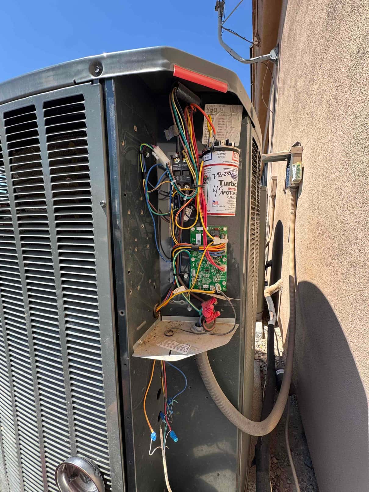 Outdoor condenser control compartment open, showing contactor, control board, wiring, and a motor run capacitor.