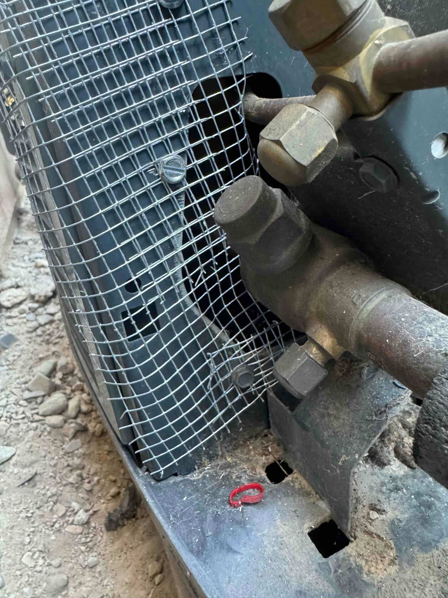 Outdoor condenser refrigerant service valves and copper lines beside a metal mesh screen and base pan.