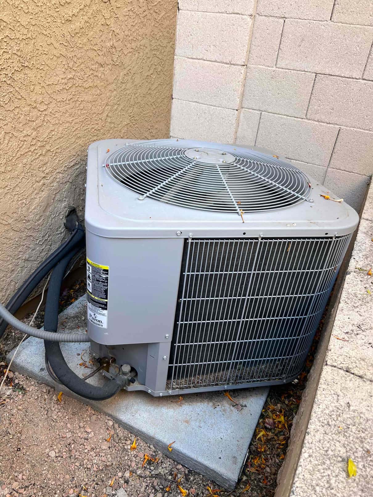 Outdoor condenser unit on a concrete pad with refrigerant lines and service valves visible near the wall.