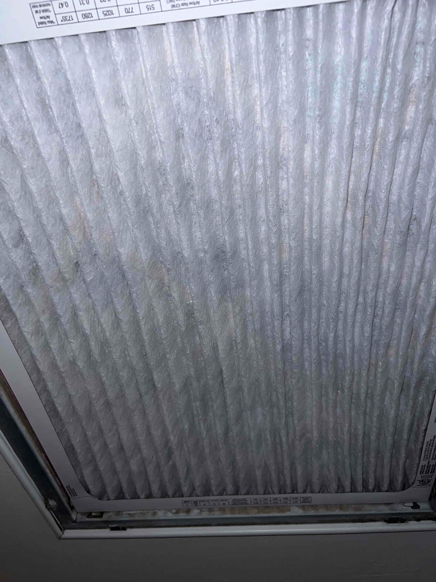 Pleated air filter installed in a ceiling return grille, viewed close-up with frame and edge labeling visible.