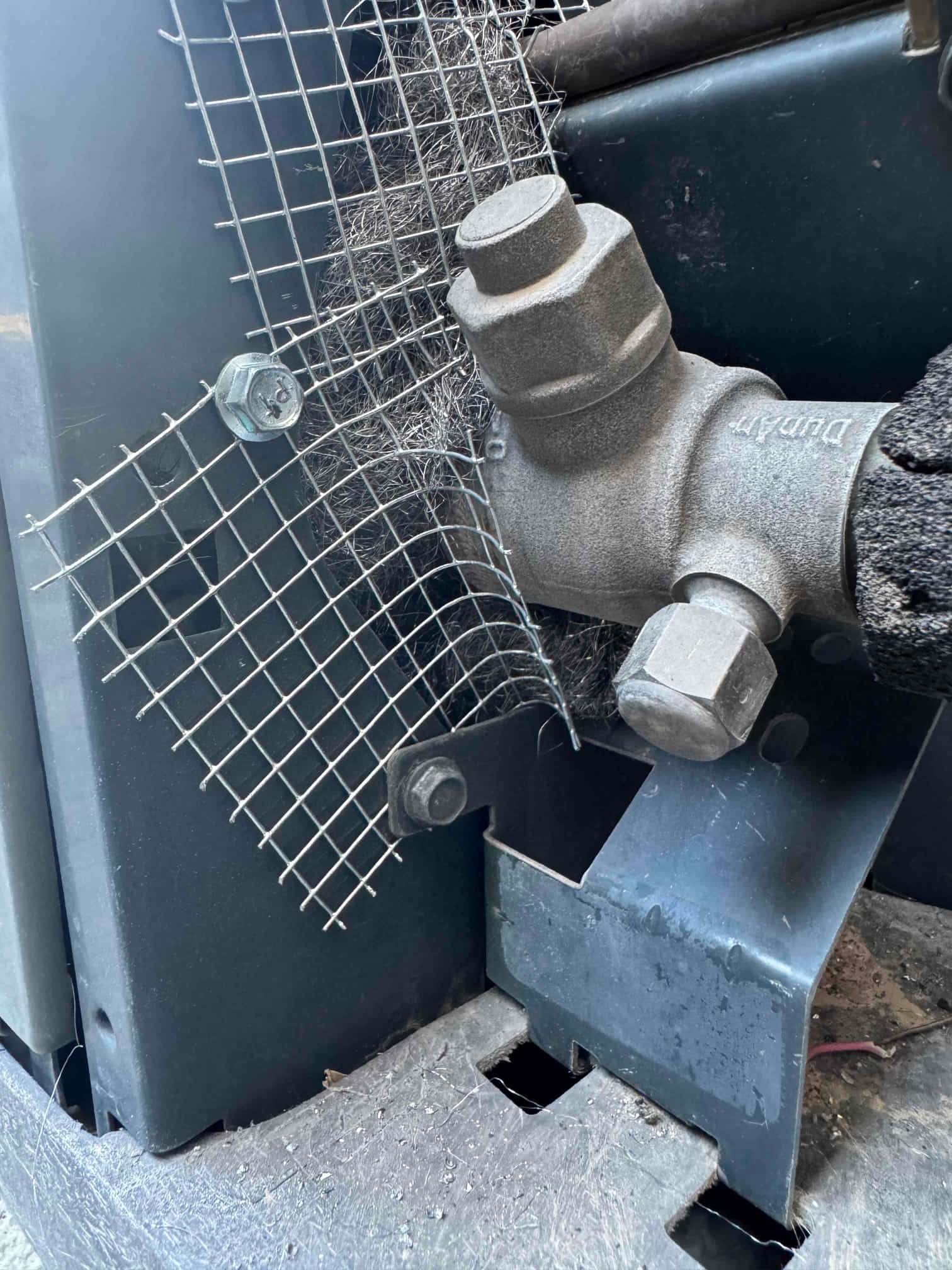 Refrigerant service valve with hex caps, adjacent to metal mesh and steel wool at unit corner.