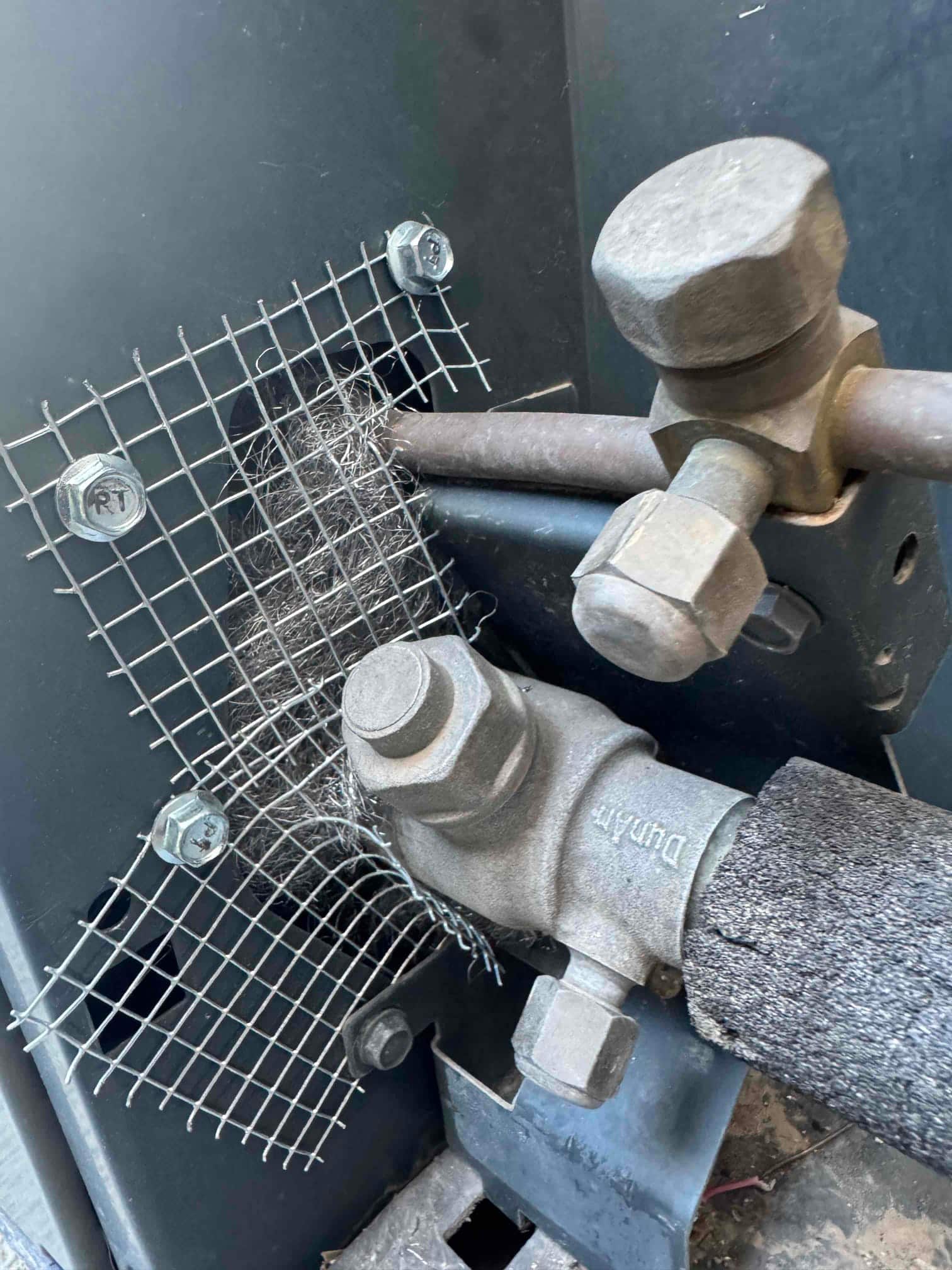 Refrigerant service valves and insulated suction line at an outdoor unit, with a metal mesh screen fastened over an opening.