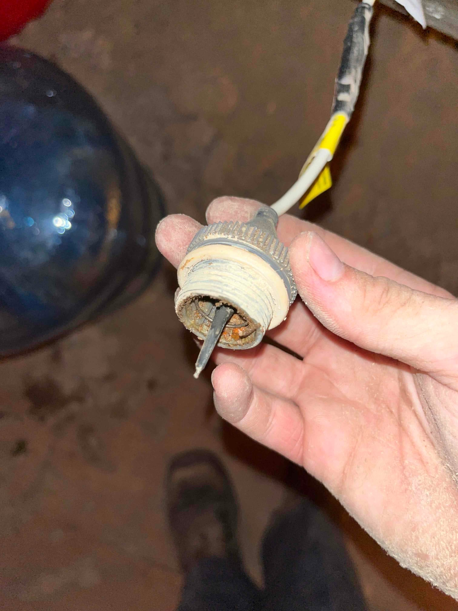 Technician holds a dusty threaded plastic fitting with a metal blade and corrosion inside, attached to a two-conductor cable.