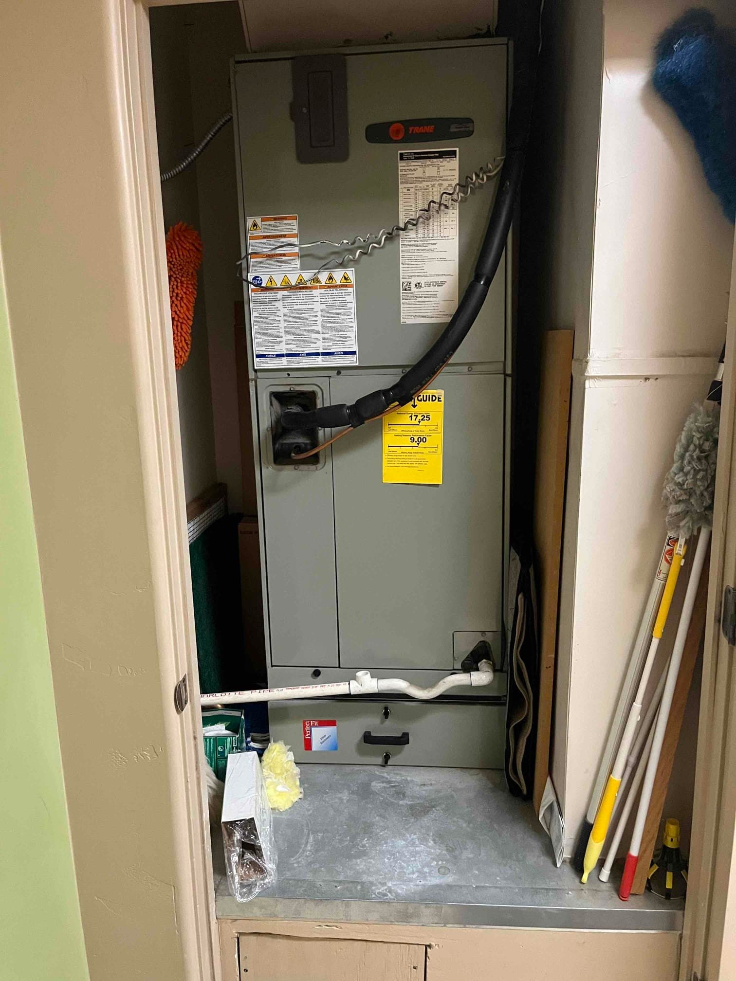 Vertical indoor air handler in a closet with insulated refrigerant line and condensate drain piping visible at the base.