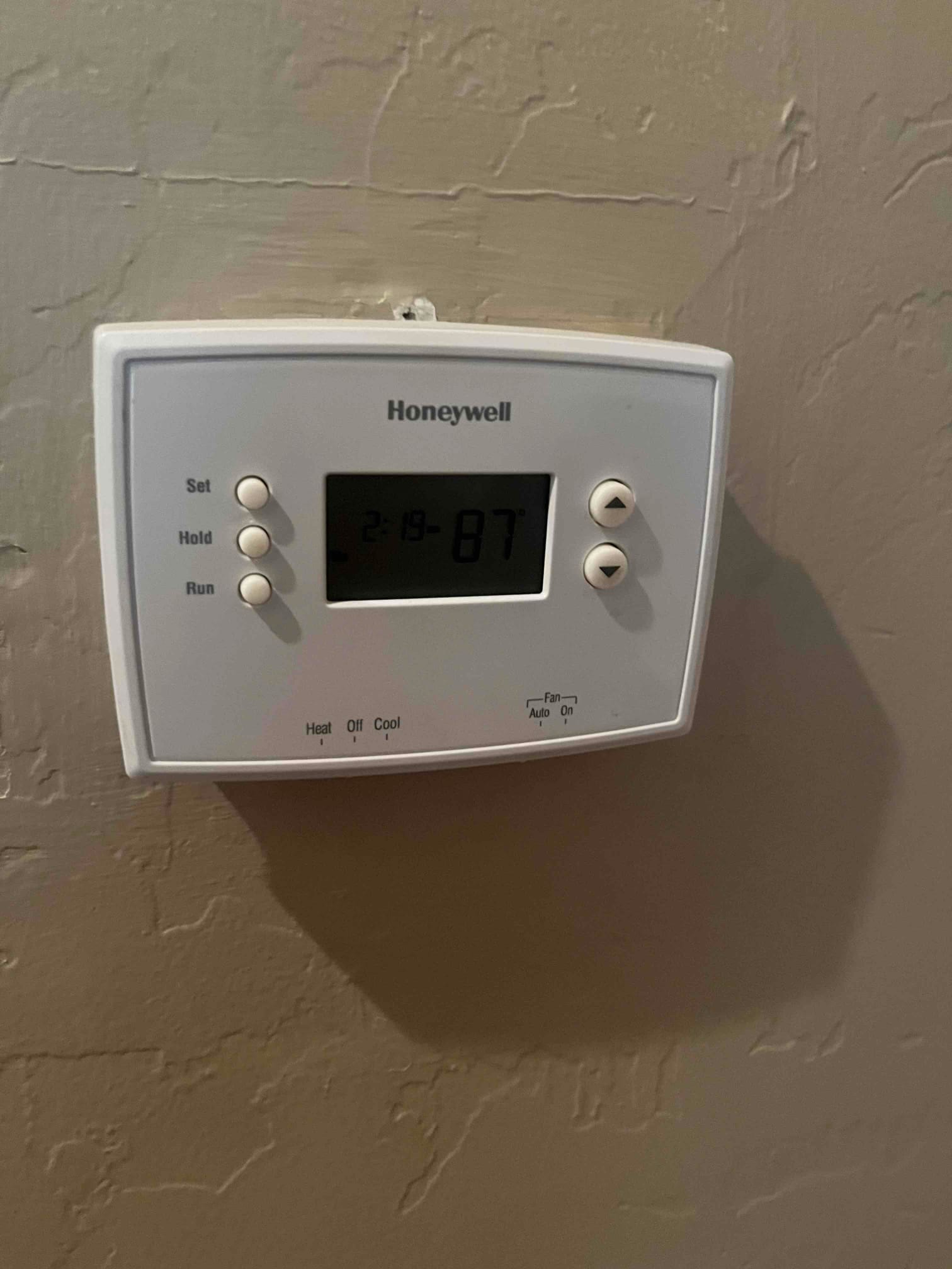 Wall-mounted digital thermostat shows 87° with time displayed, alongside system heat/cool and fan auto/on selectors.