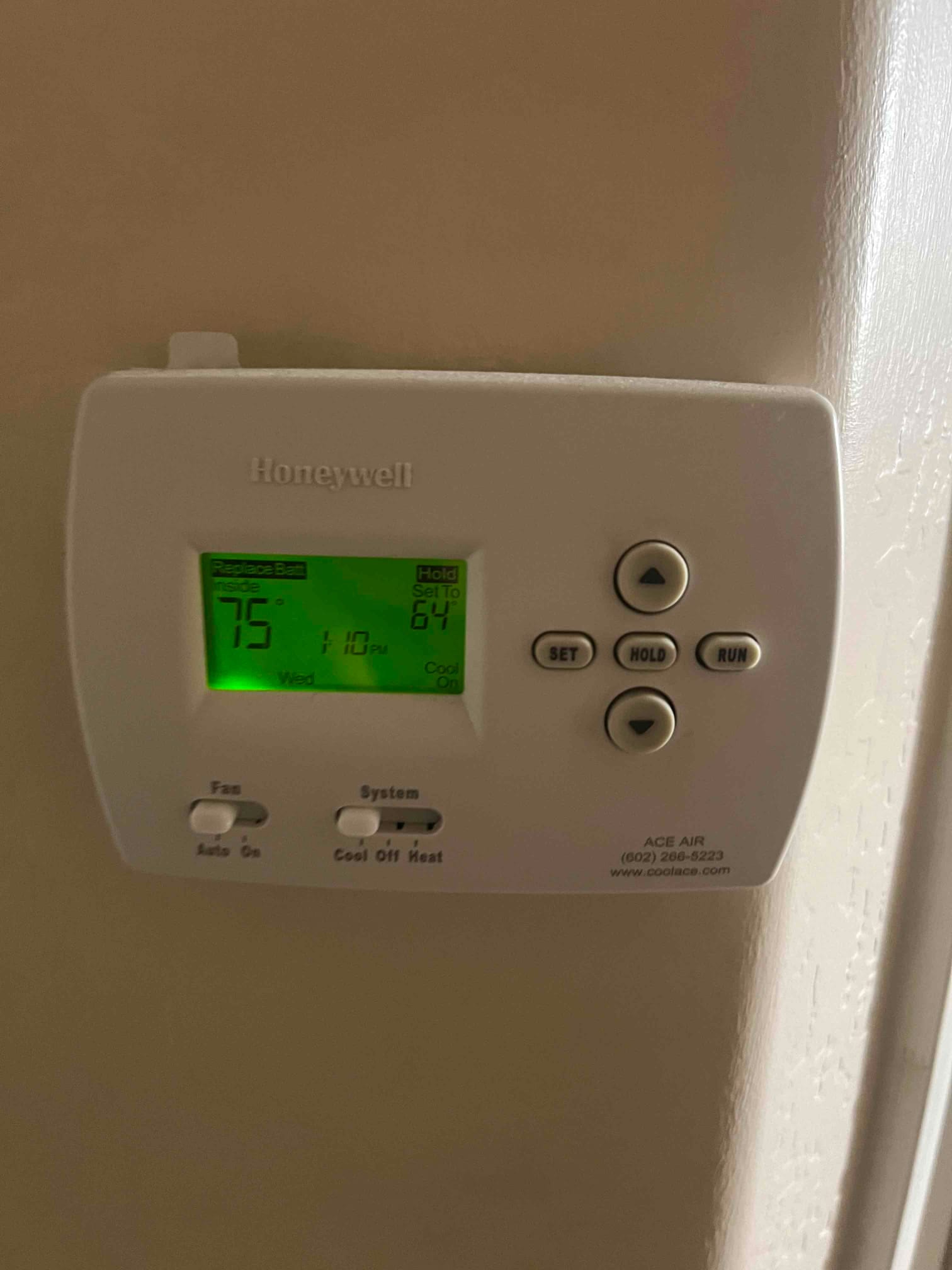 Wall-mounted digital thermostat shows inside temperature 75°F and setpoint 64°F with system switch on Cool.