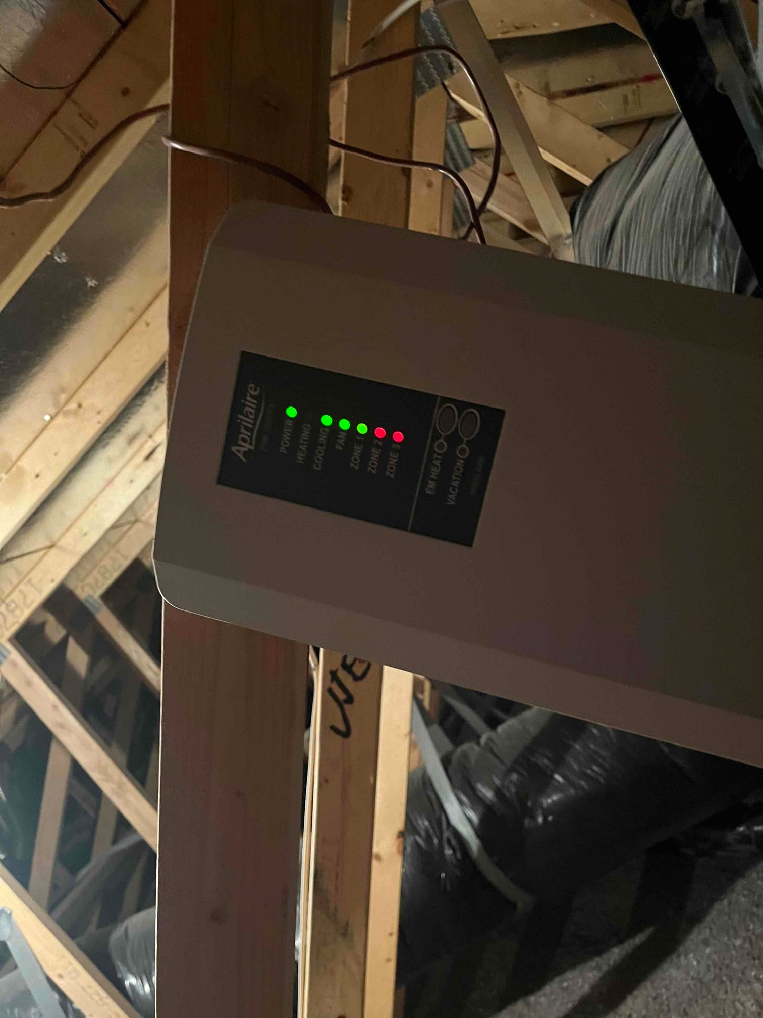 Zoning control panel mounted on attic framing with multiple status LEDs illuminated for power, heating, cooling, and zones.