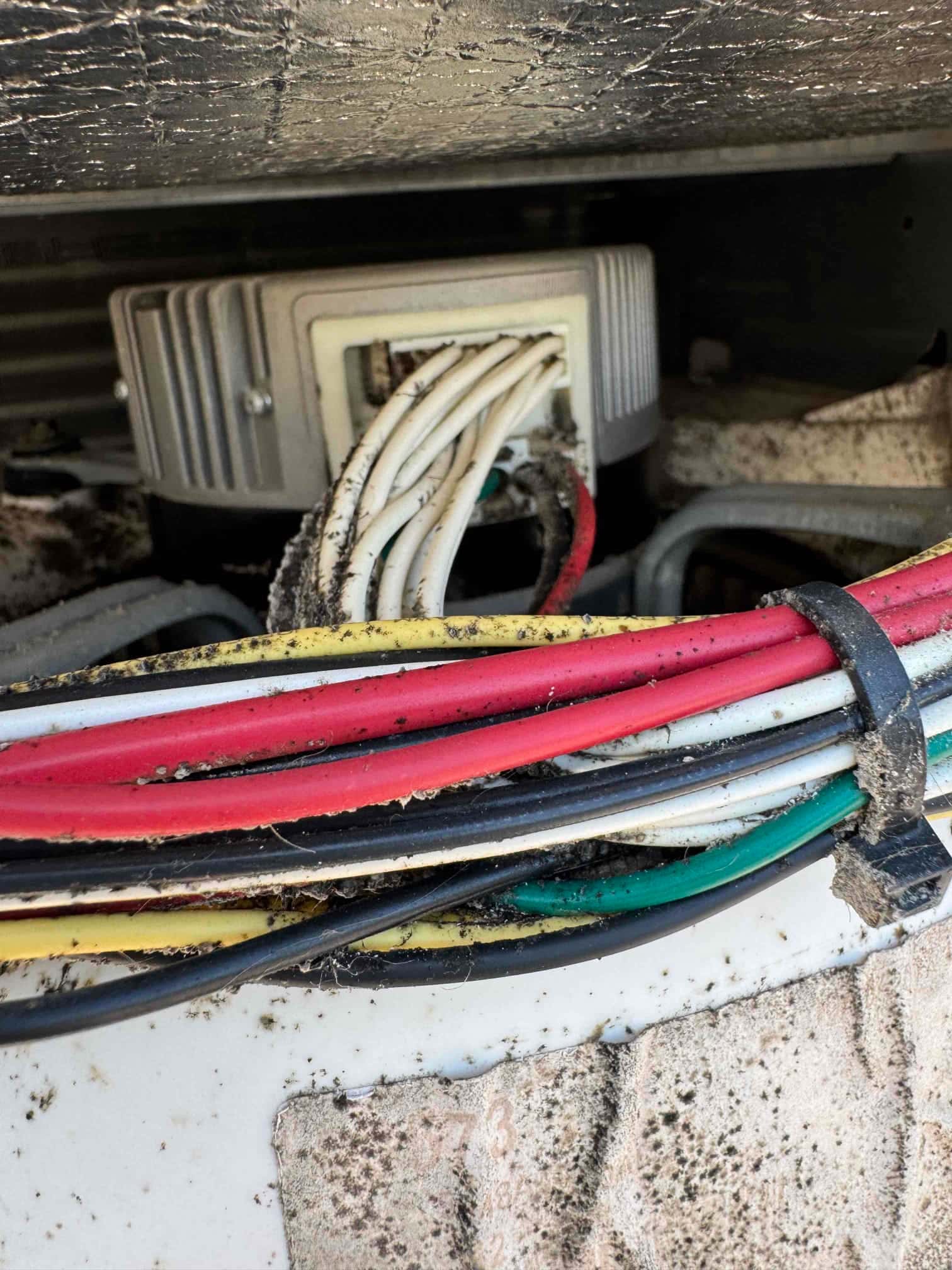 Bundle of control and power wires entering a plastic connector inside the unit cabinet, with visible dust and debris.