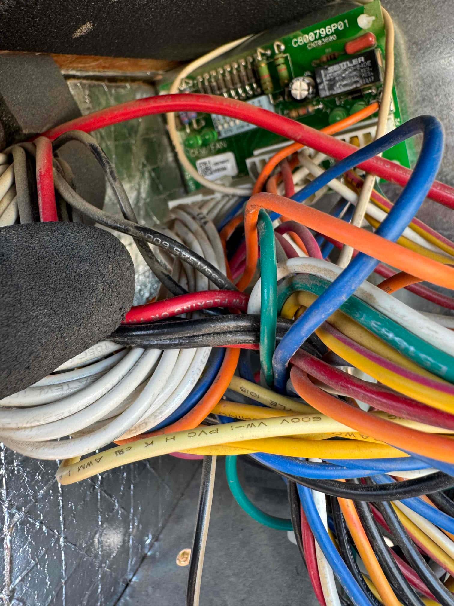 Control board inside HVAC unit with numerous colored wires bundled and connected to terminals.