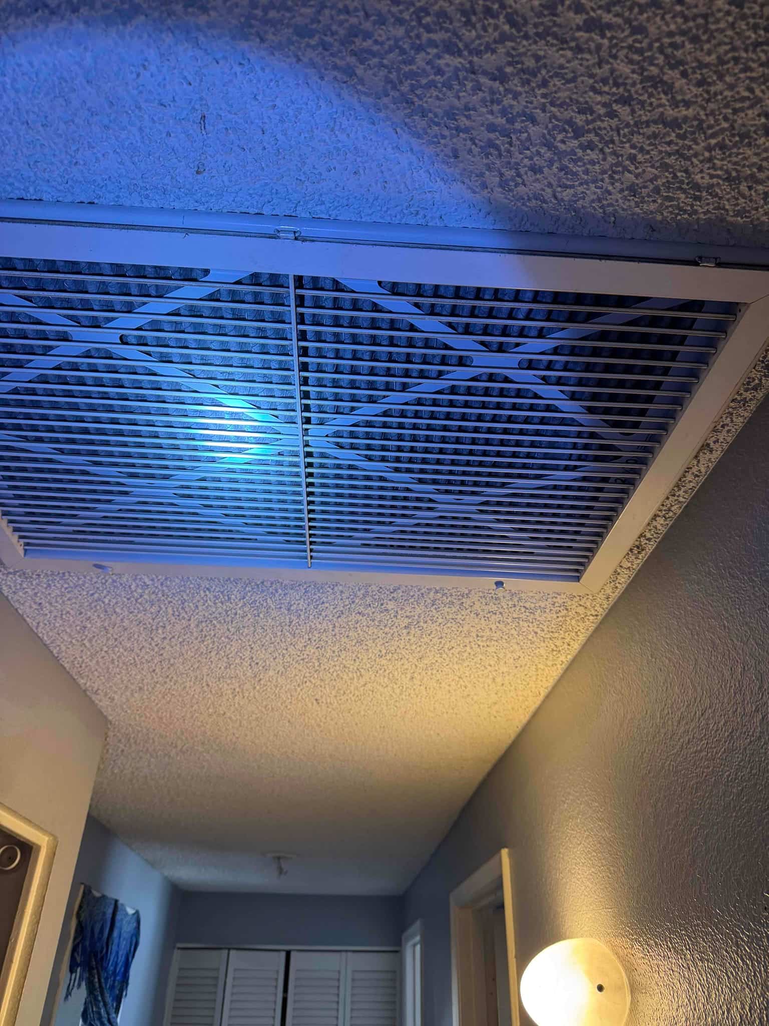 Ceiling return air grille in a hallway with filter visible behind the slats, illuminated by work light.