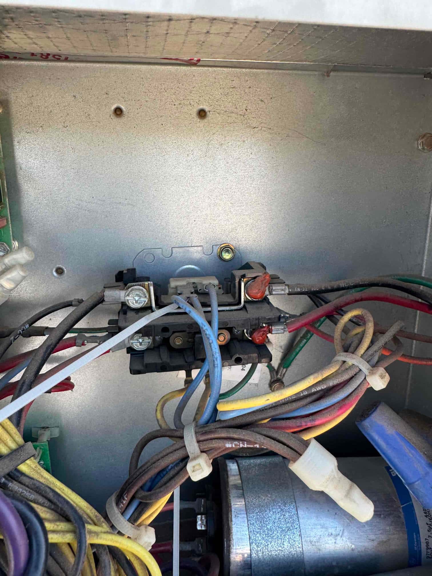 Contactor with multiple wiring connections inside the condenser control panel, with bundled conductors and a cylindrical run capacitor visible at the bottom.