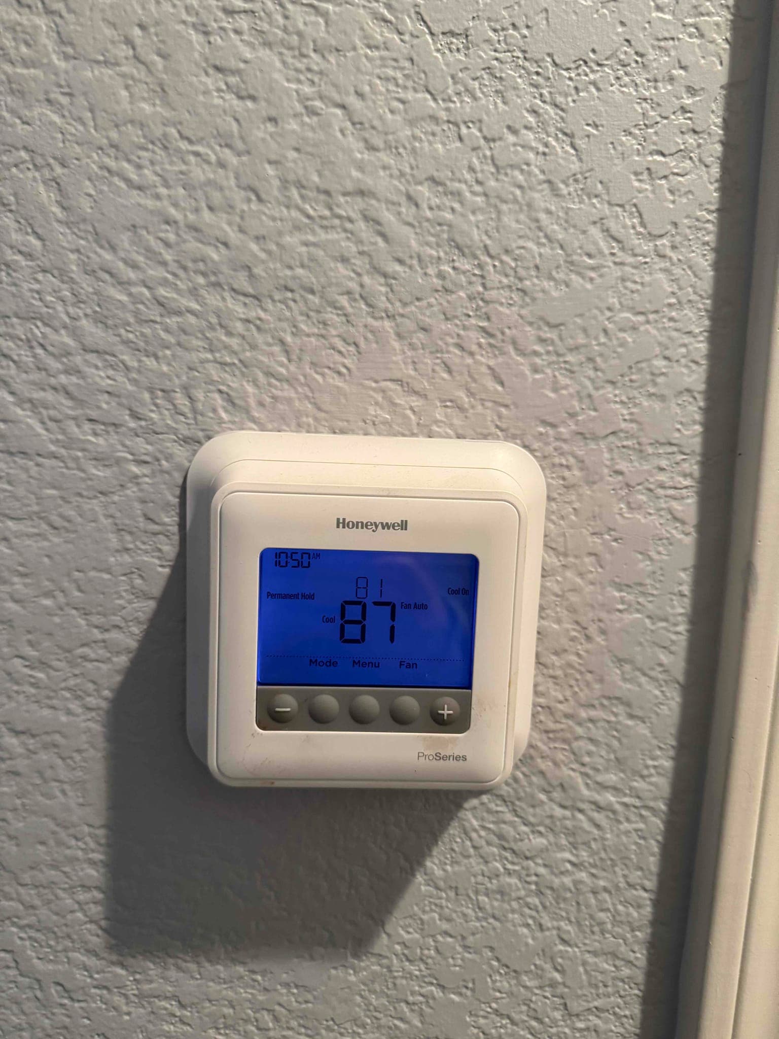 Digital thermostat on the wall shows 87 with cool mode active and fan in Auto.