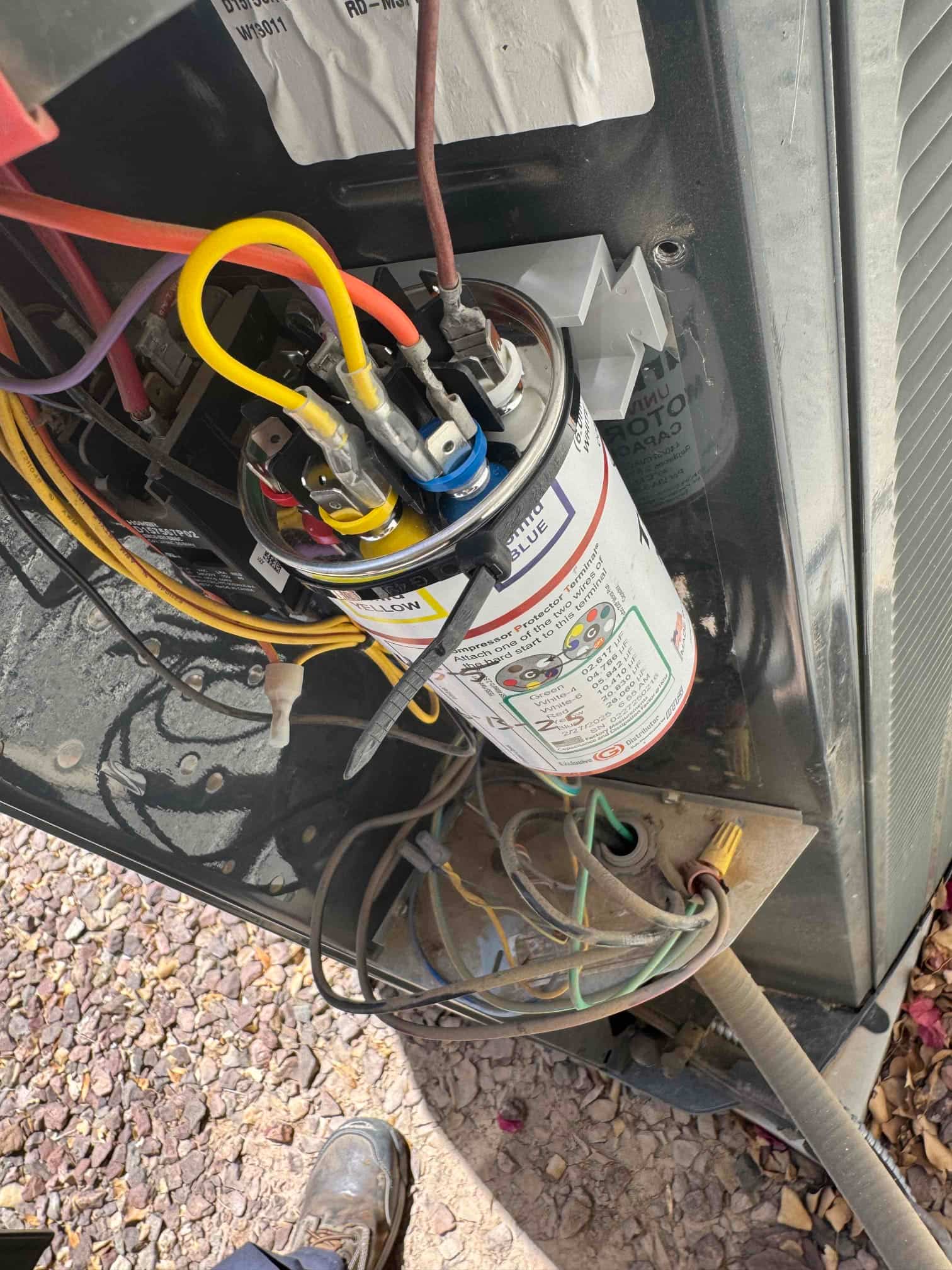 Dual-run capacitor with color-coded terminals and connected wires inside the outdoor condenser electrical compartment.
