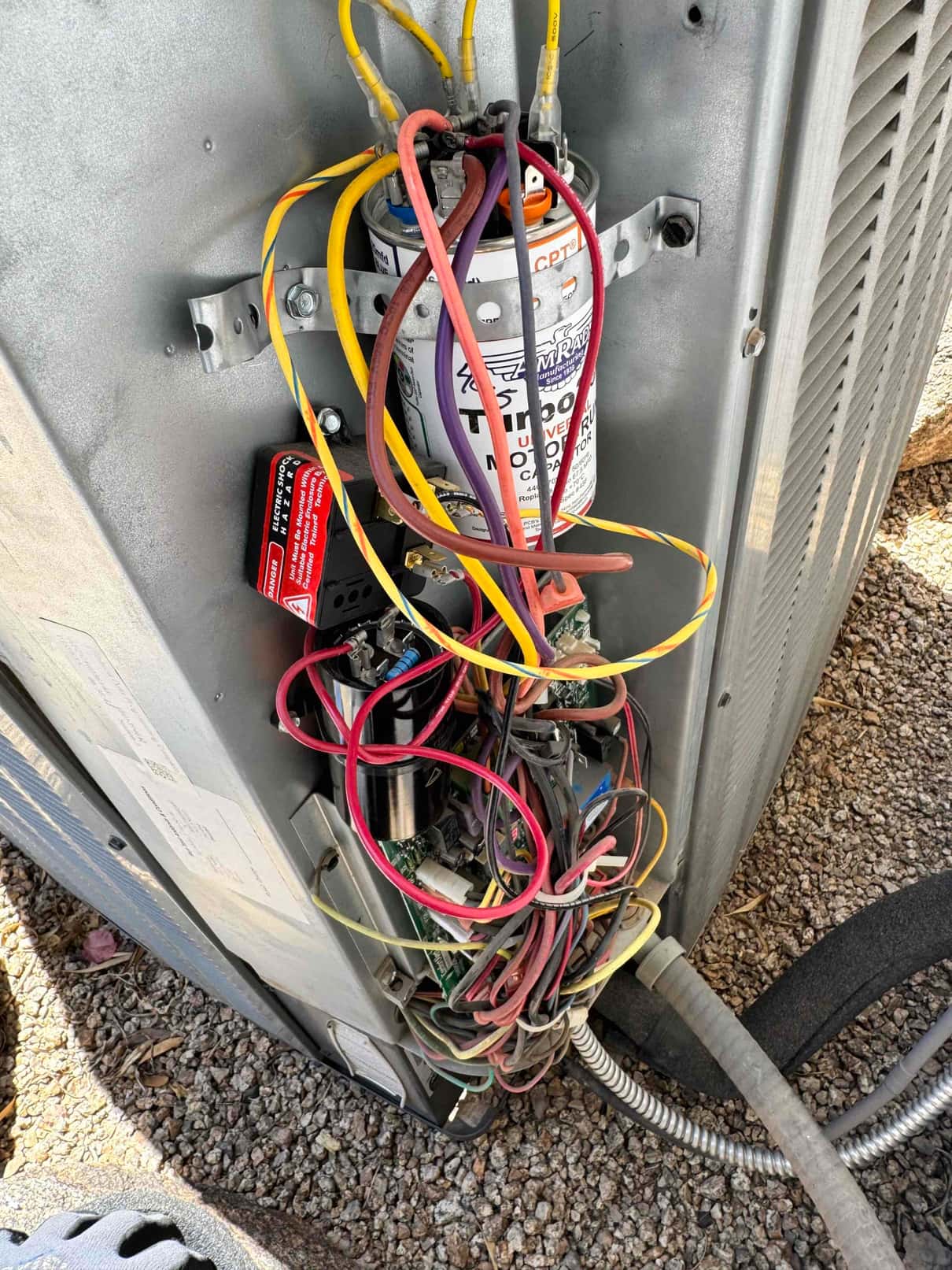 Dual-run capacitor with multiple wires connected, contactor, and wiring bundle inside an outdoor condenser control compartment.
