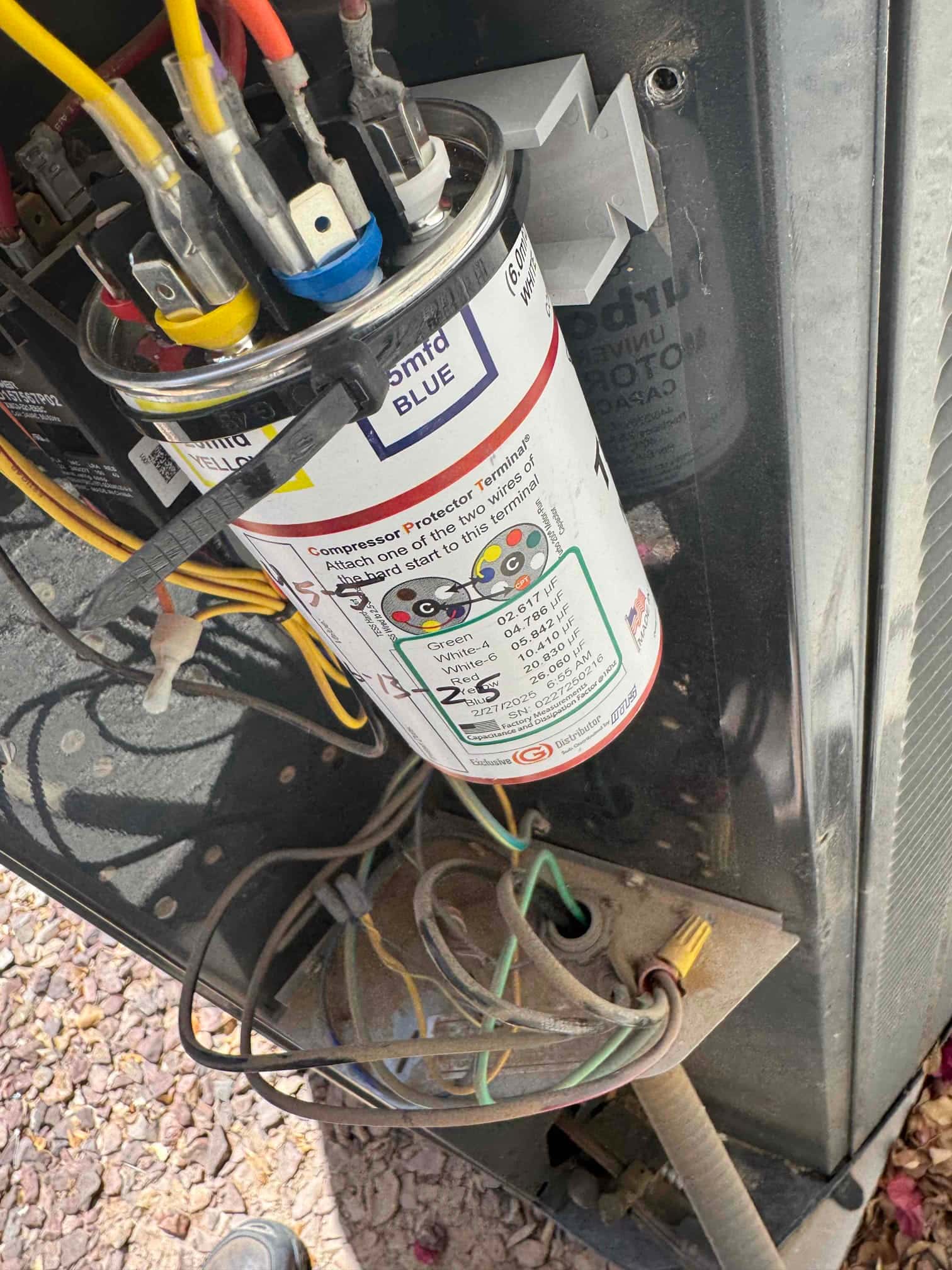 Dual-run capacitor in the outdoor condenser compartment, with multiple colored wires connected to its labeled terminals.