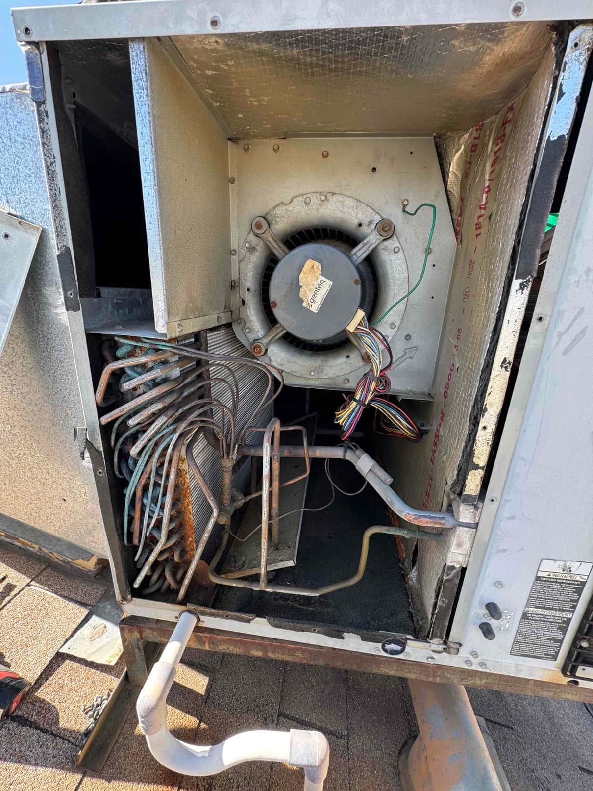 Open air handler compartment showing blower motor assembly, evaporator coil with oxidized copper tubing, connected drain piping, and wiring harness.