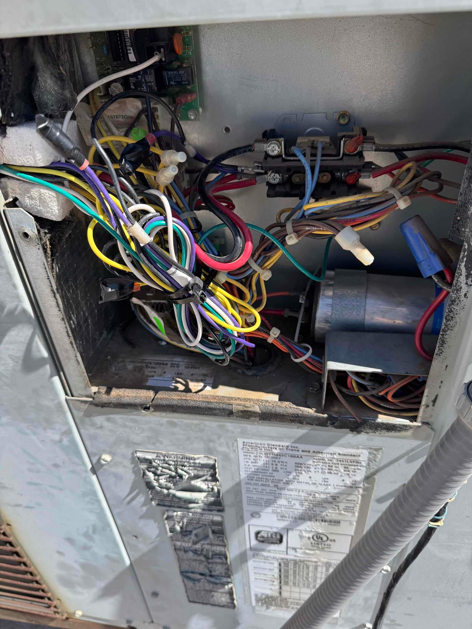 Outdoor condenser control compartment open, showing contactor, run capacitor in bracket, and multiple connected wires.
