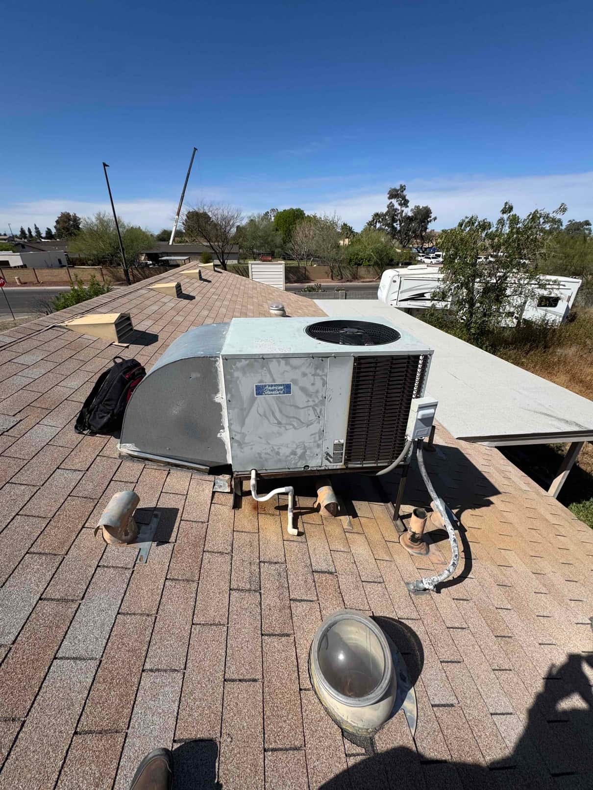 Rooftop package HVAC unit on shingle roof with exposed refrigerant lines, condensate drain, and service disconnect.