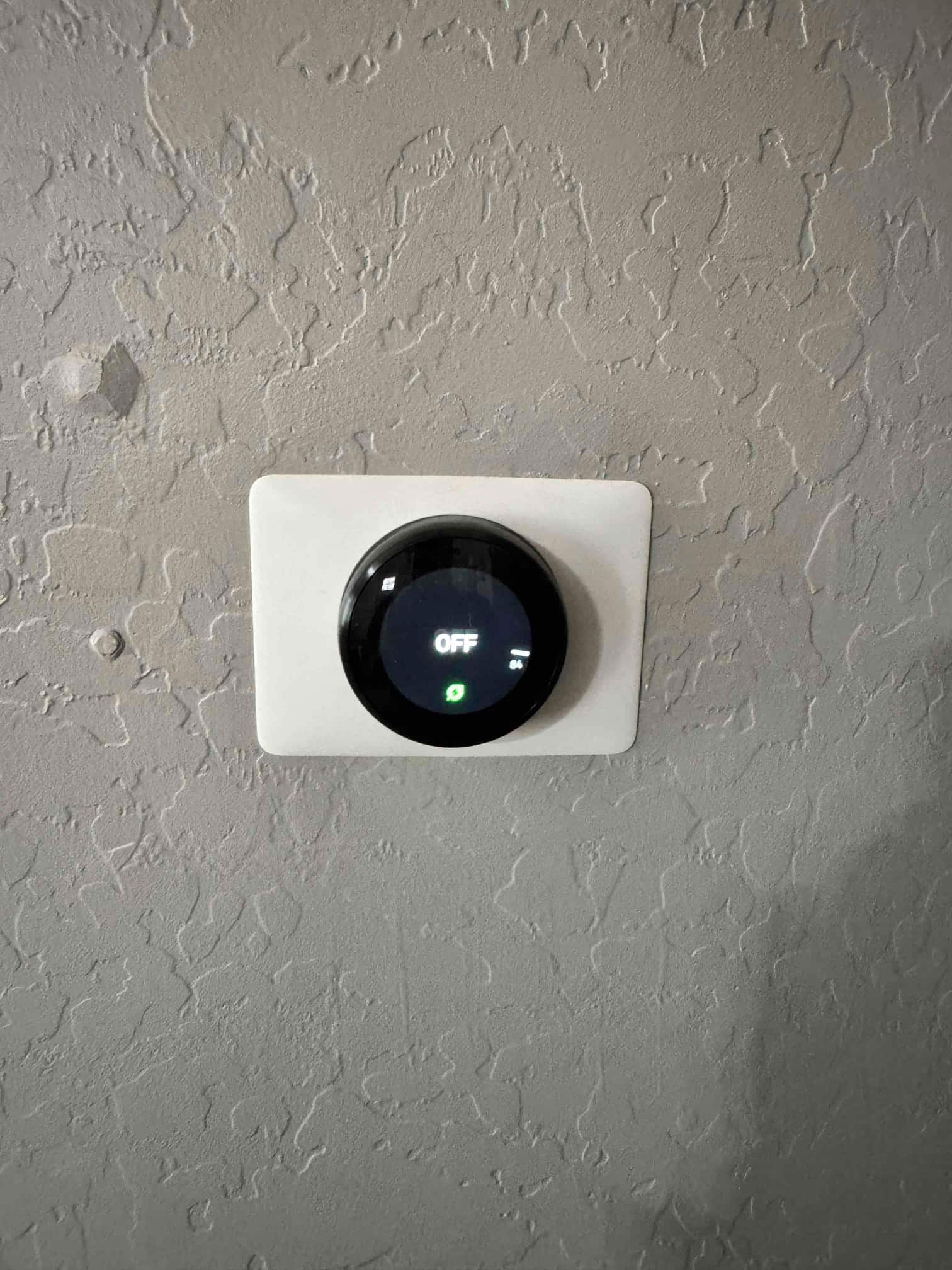Smart thermostat mounted on wall showing system set to Off with illuminated green leaf icon.