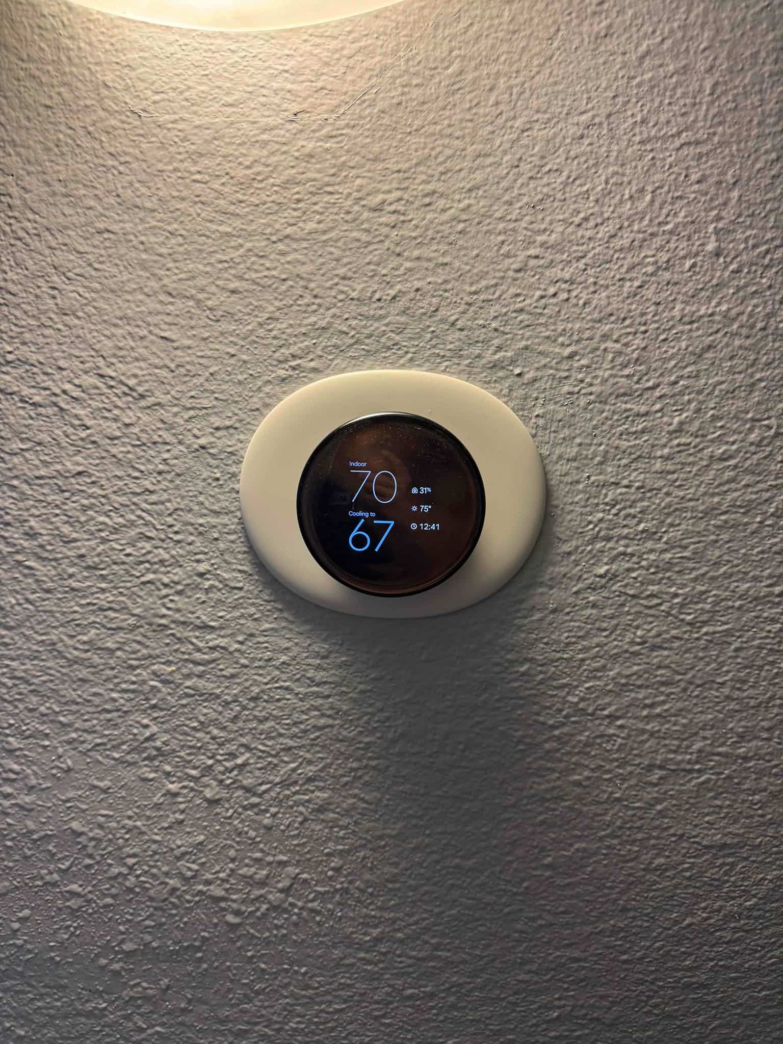 Wall-mounted round digital thermostat shows indoor temperature 70°F and cooling set to 67°F, with time display visible.
