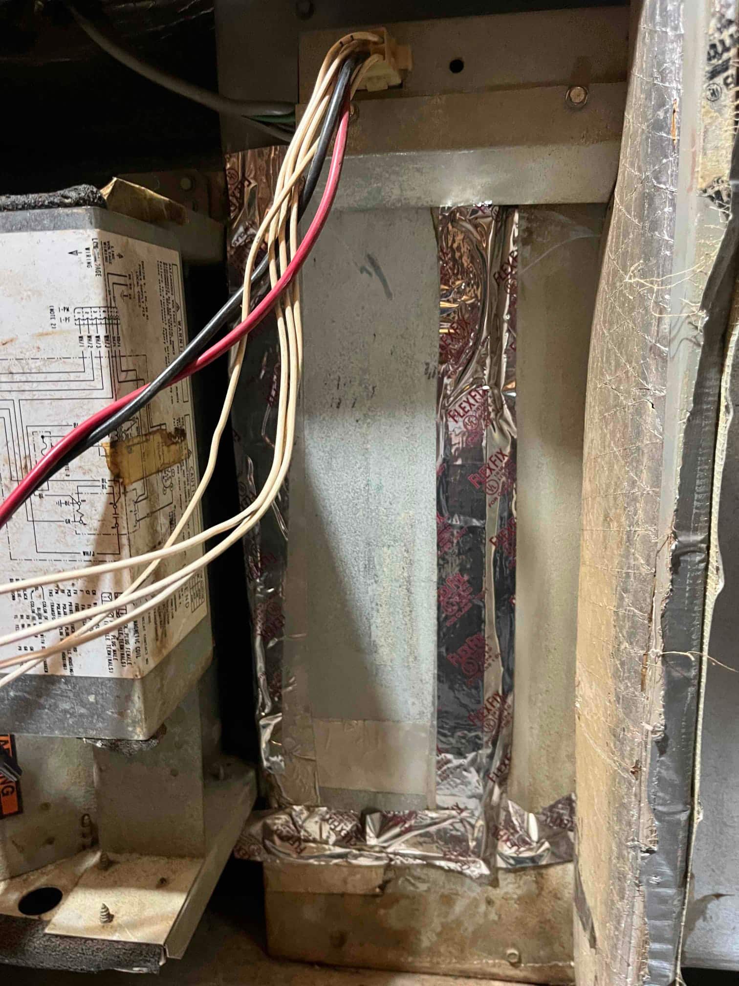 Air handler interior shows control box with wiring diagram, bundled low-voltage wires, and foil tape sealing a vertical duct panel.