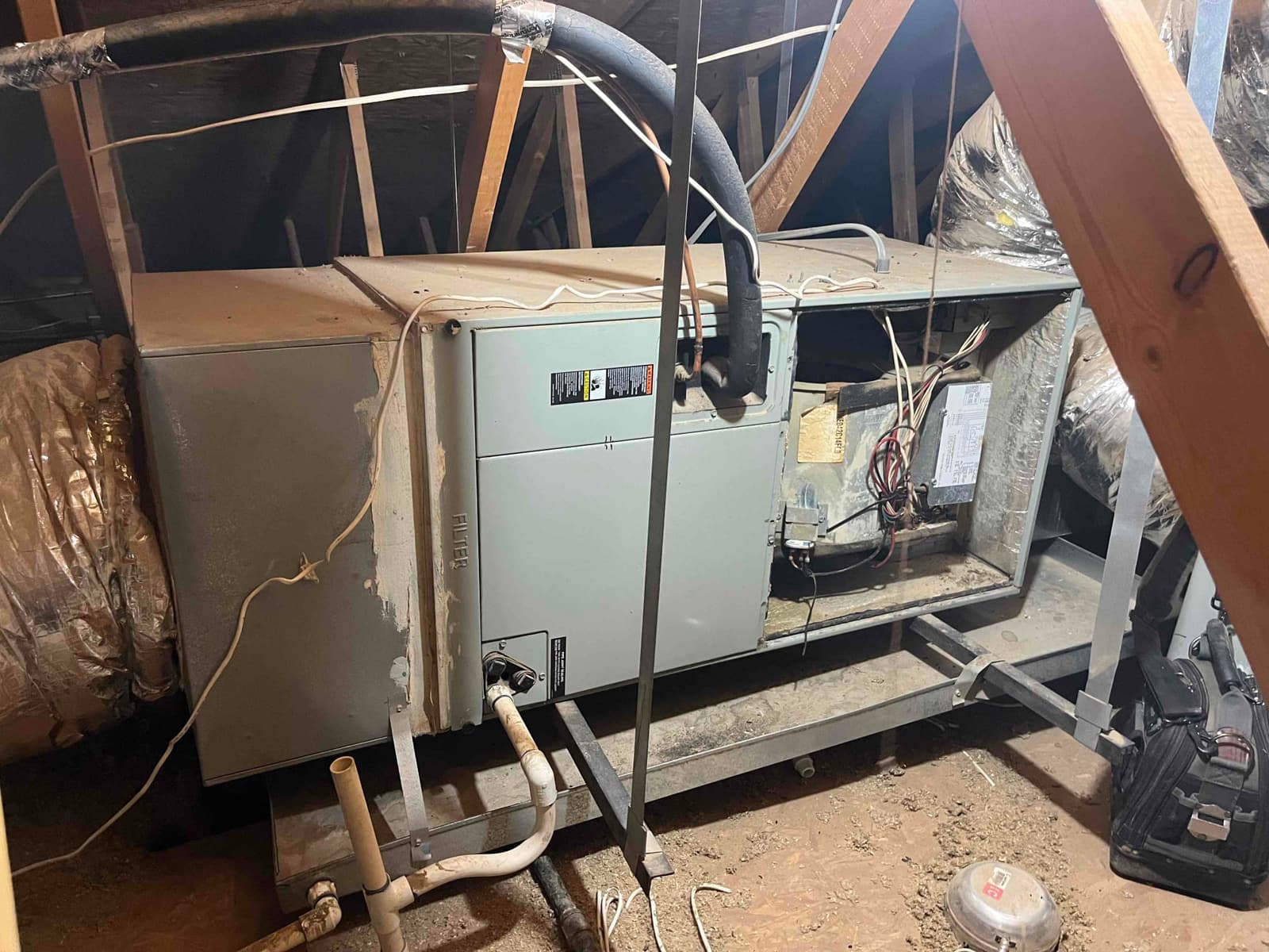 Attic air handler with access panel open, showing blower compartment wiring, condensate piping, and connected flexible ductwork.