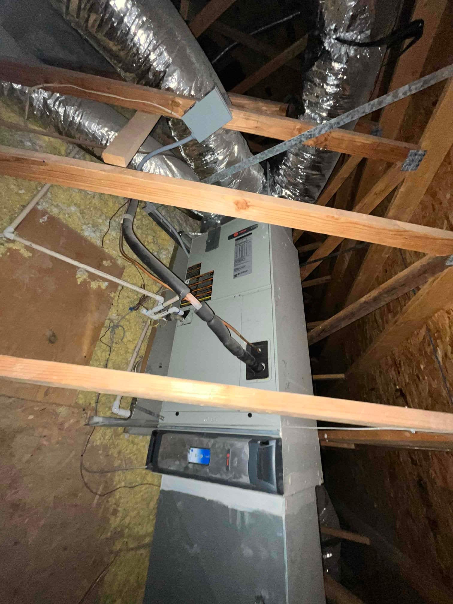 Attic air handler with insulated refrigerant lines, PVC condensate drain, and connected flex ductwork visible between ceiling joists.