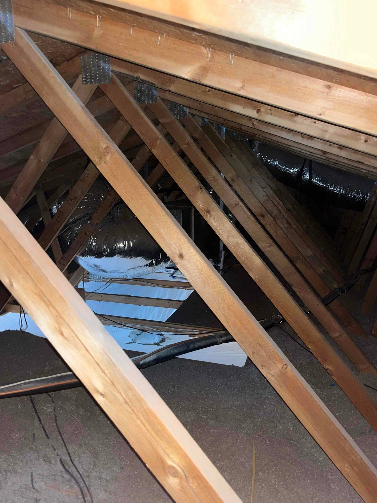 Attic framing with insulated flexible air ducts and a black insulated line running across the space.