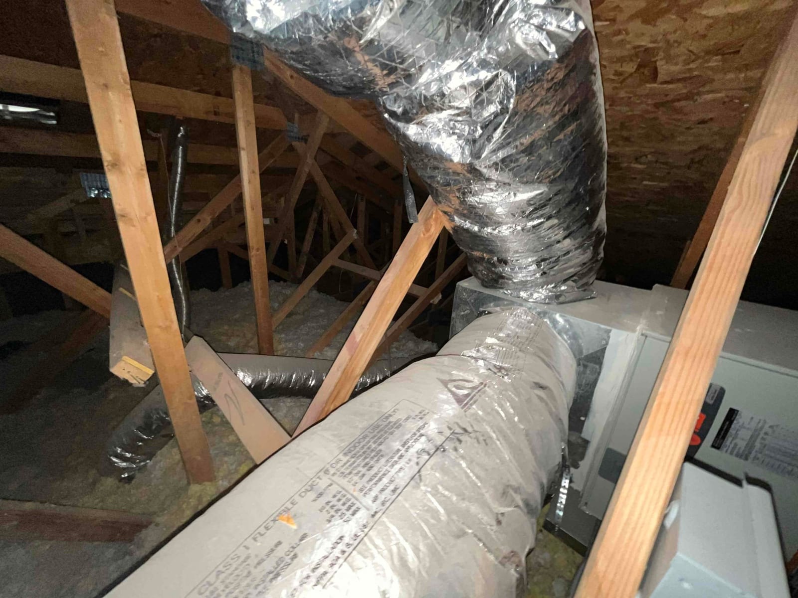 Attic installation showing air handler with metal plenum connected to insulated flexible ductwork between trusses.