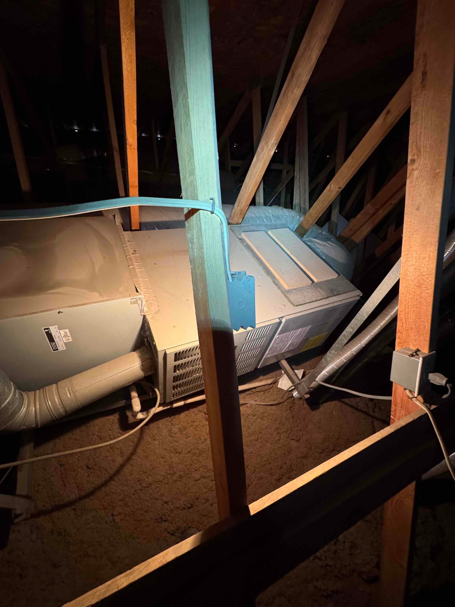 Attic-mounted horizontal air handler with connected ductwork, condensate drain, and service panels visible among truss framing.