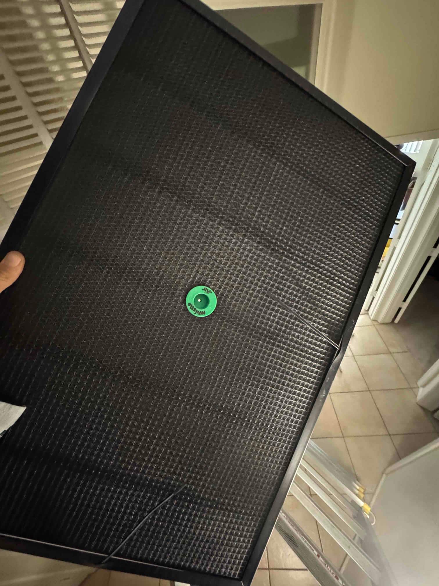 Black HVAC return grille filter panel with green pull tab, shown indoors near a ladder.