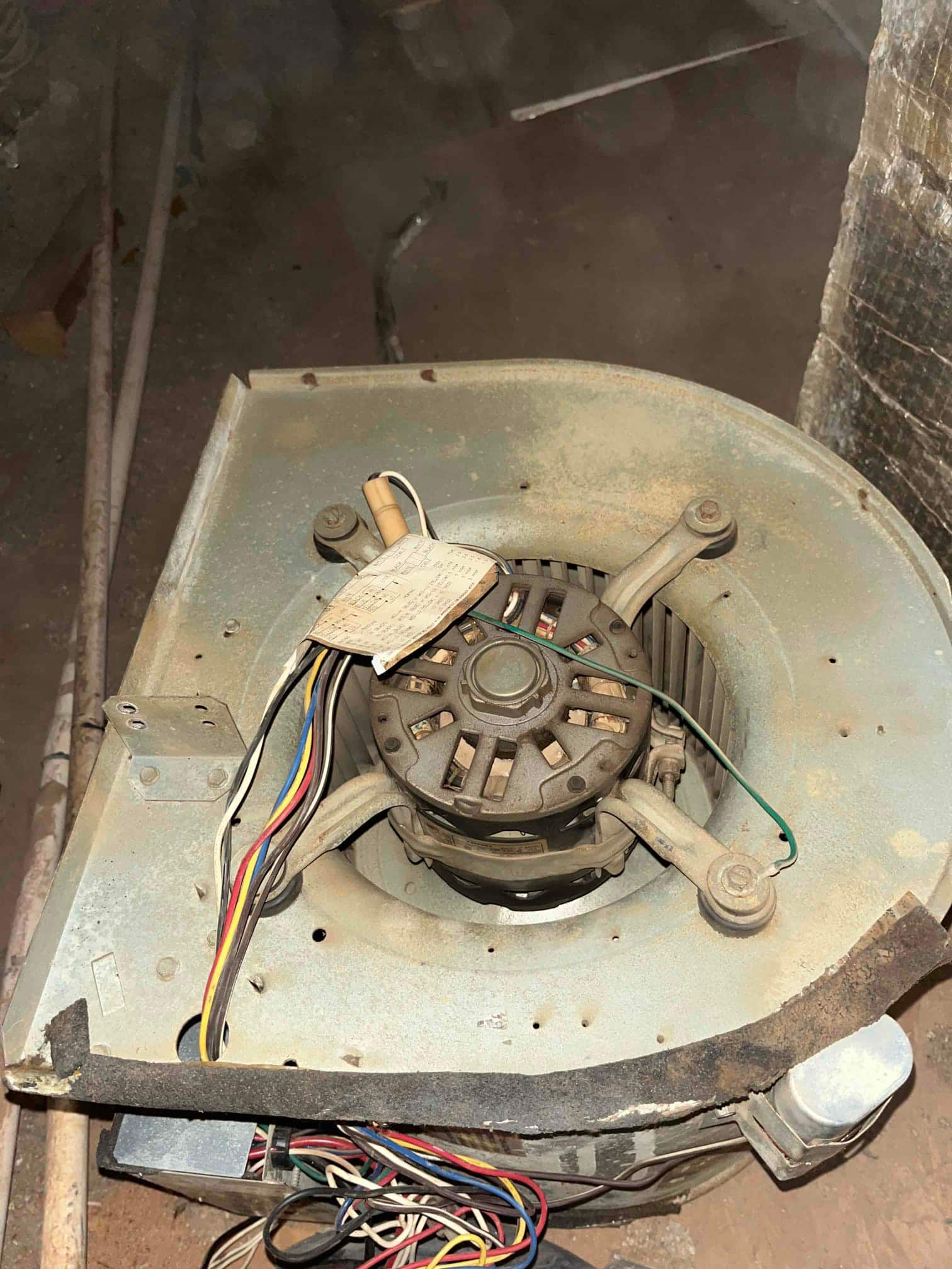 Blower assembly on the floor shows the blower motor, squirrel-cage wheel, wiring harness, and an attached oval run capacitor with dust buildup.