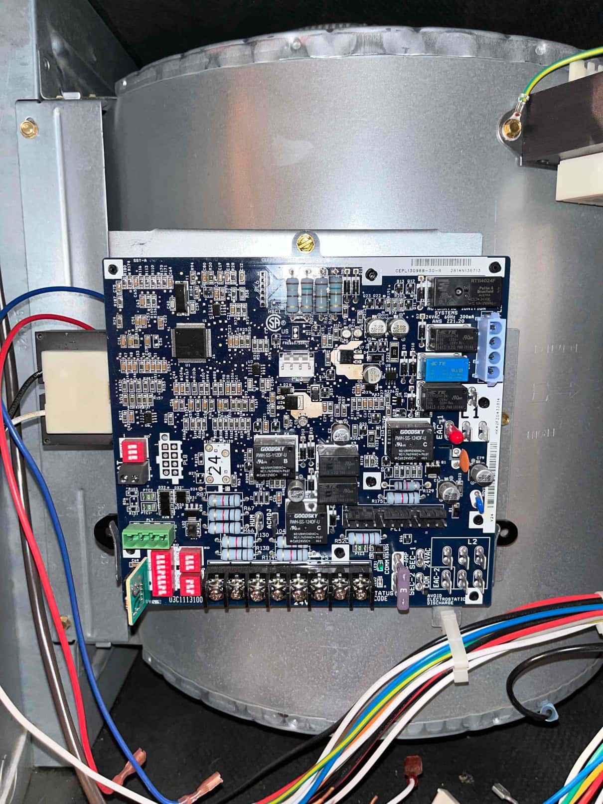 Blower compartment control board mounted on metal housing with DIP switches, terminal strip, relays, and connected low-voltage wiring.