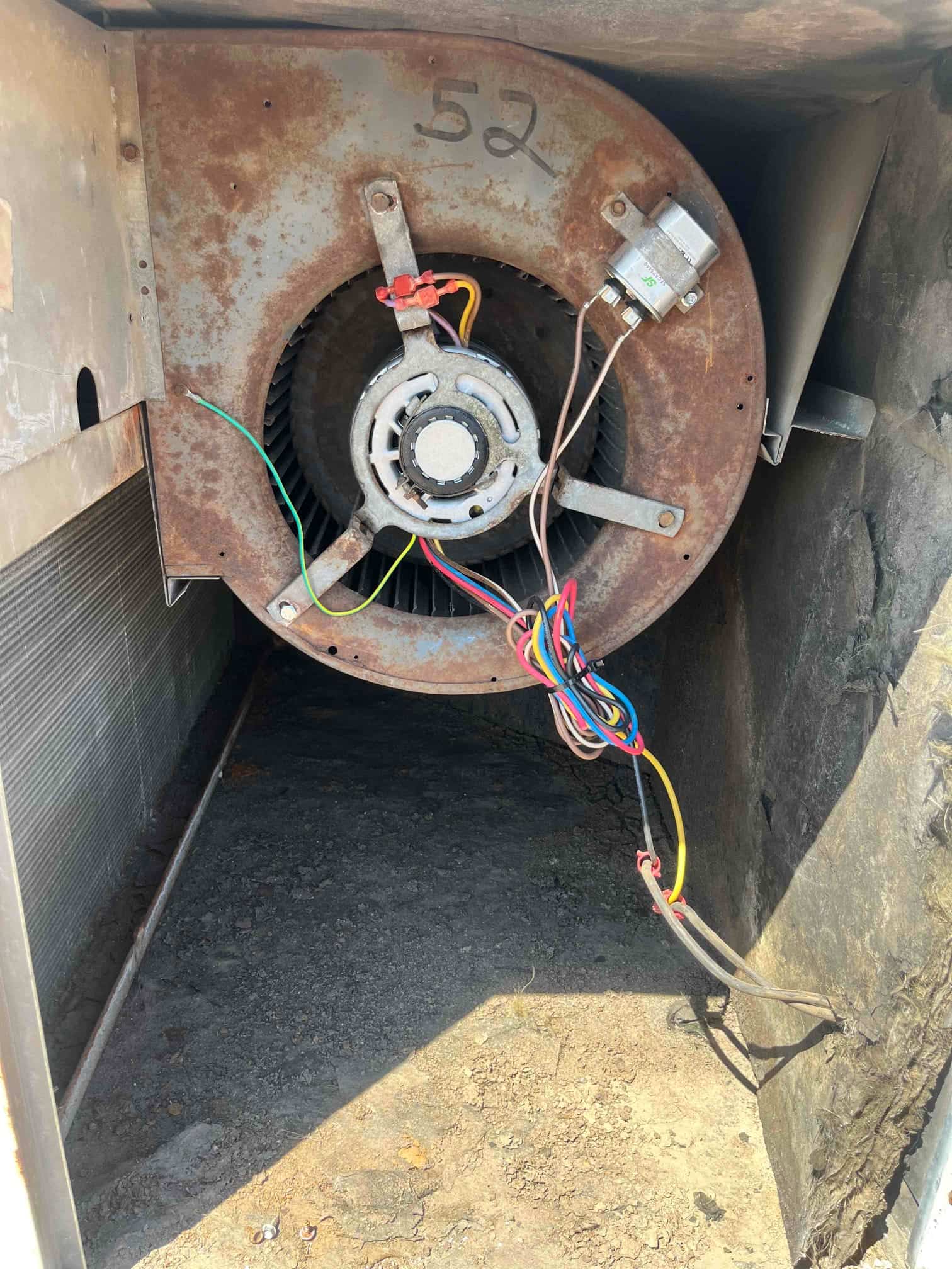 Blower motor and fan wheel inside the unit, with rusted housing, connected wiring, and a mounted run capacitor on the shroud.